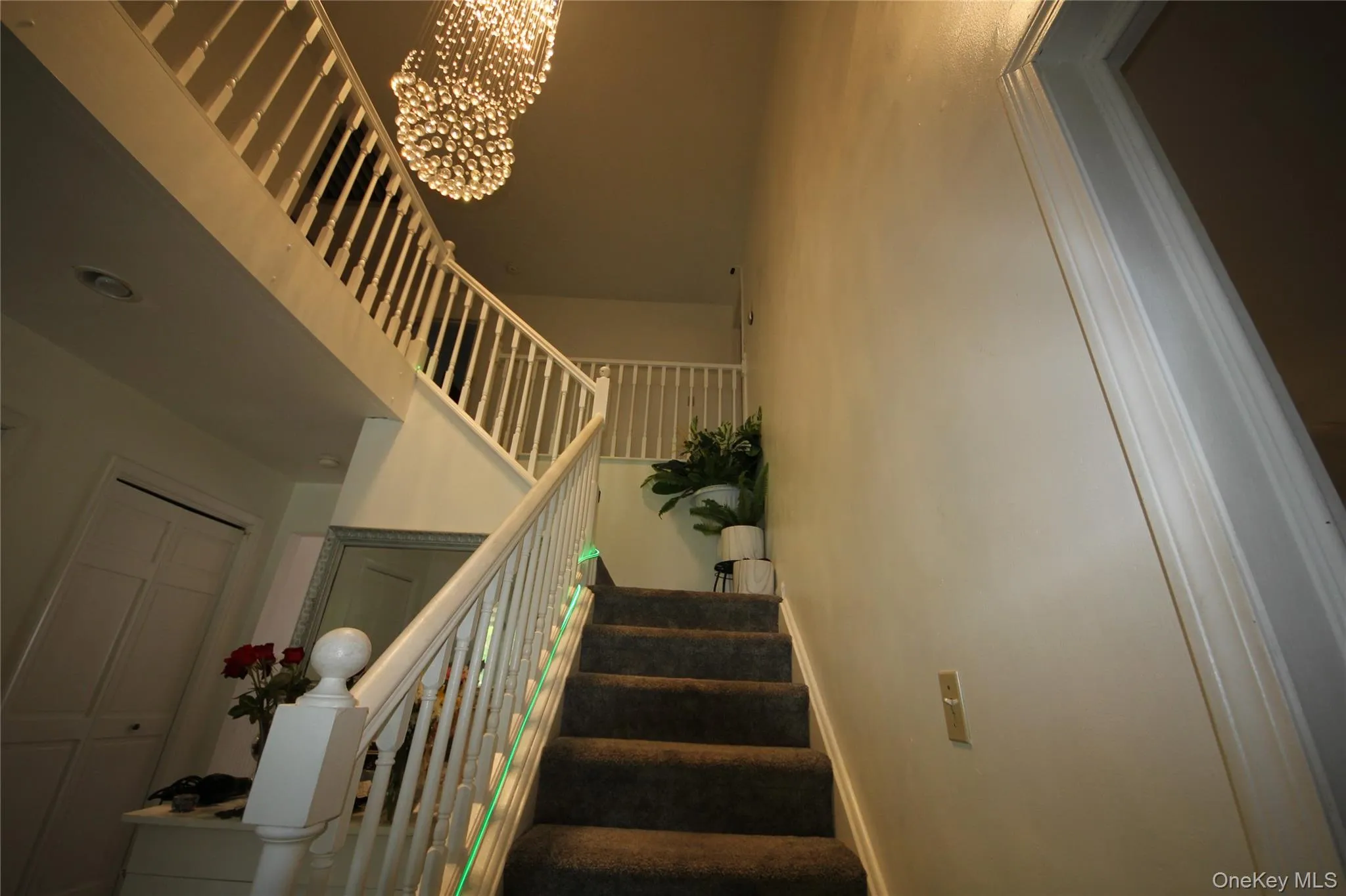 Two-story interior staircase with white balusters, carpeted treads, and a multi-tiered crystal chandelier Two-story interior staircase with white balusters, carpeted treads, and a multi-tiered crystal chandelier