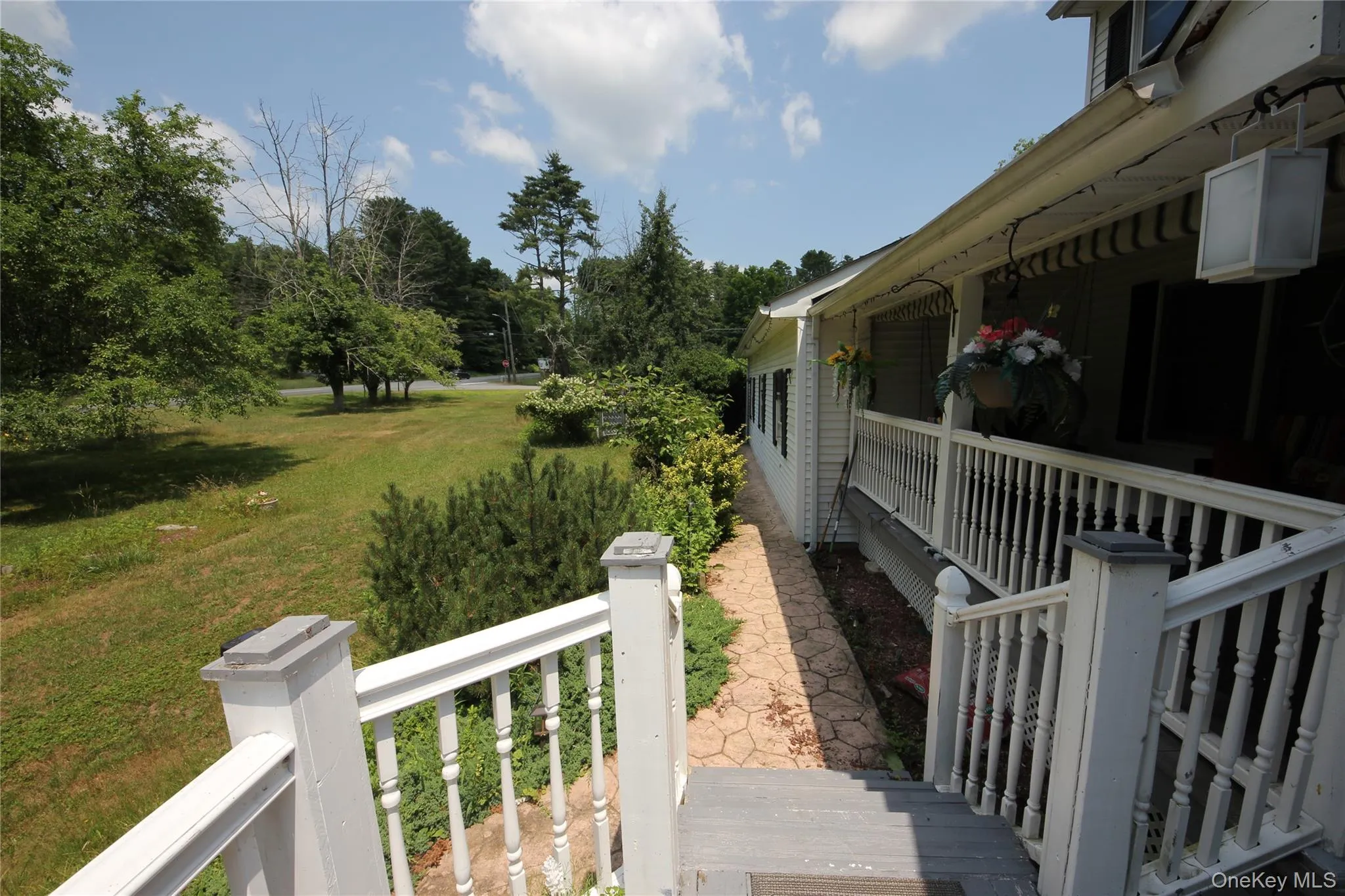 Exterior featuring white siding, a covered porch with white railing and balusters, and an adjacent stone-look pathway Exterior featuring white siding, a covered porch with white railing and balusters, and an adjacent stone-look pathway