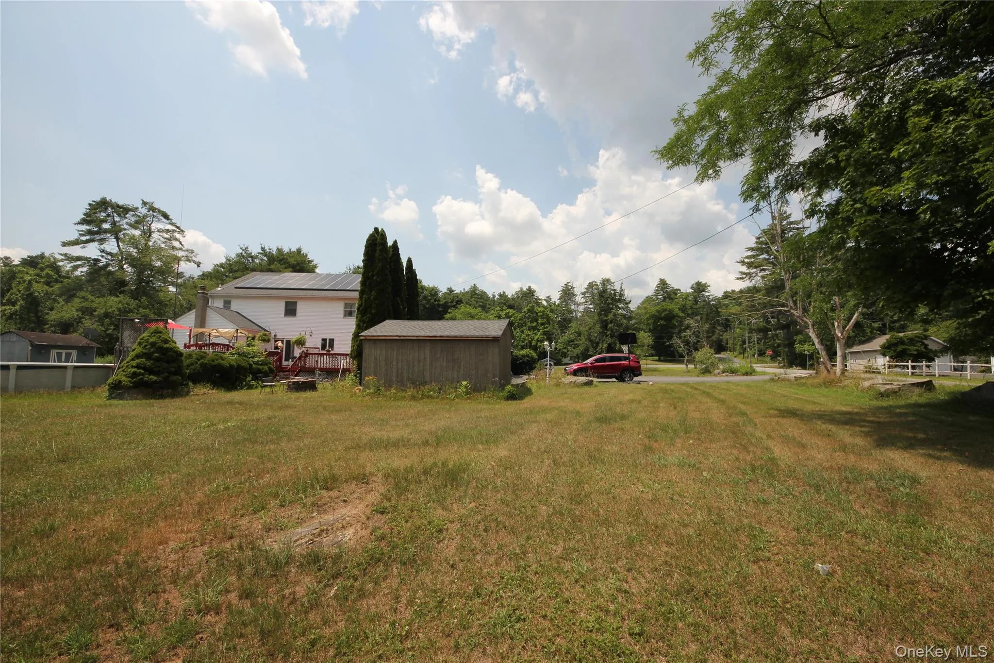 Expansive rear yard featuring a detached storage shed and a multi-level deck with red railing Expansive rear yard featuring a detached storage shed and a multi-level deck with red railing