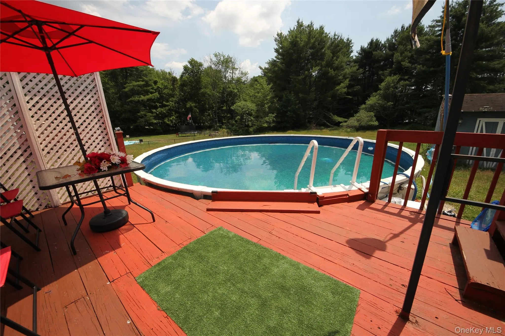 Above-ground pool with integrated ladder access, surrounded by a red-stained wood deck Above-ground pool with integrated ladder access, surrounded by a red-stained wood deck