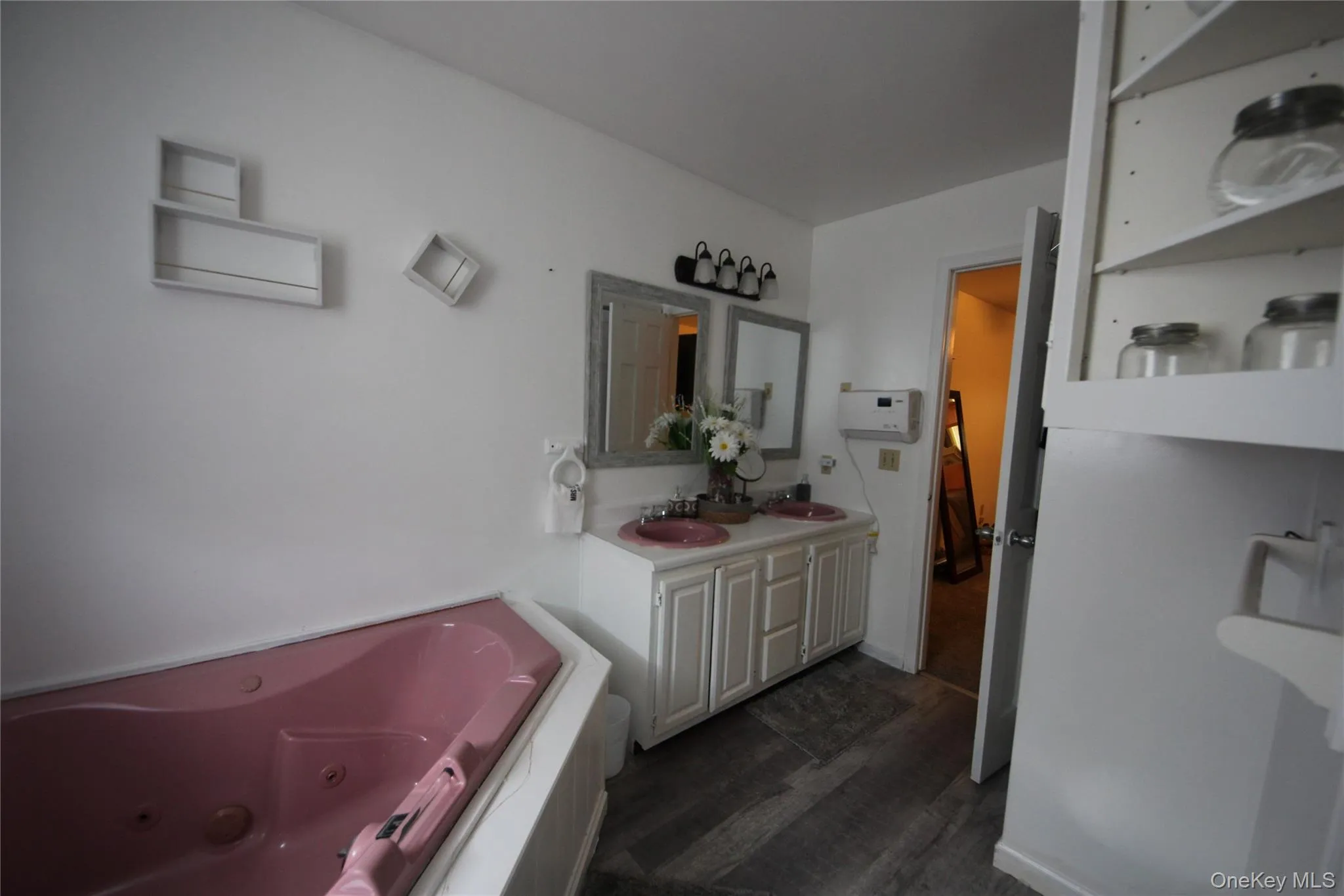 Bathroom featuring a corner jetted soaking tub, double vanity with two sinks, wall-mounted mirrors, and wood-finish flooring Bathroom featuring a corner jetted soaking tub, double vanity with two sinks, wall-mounted mirrors, and wood-finish flooring