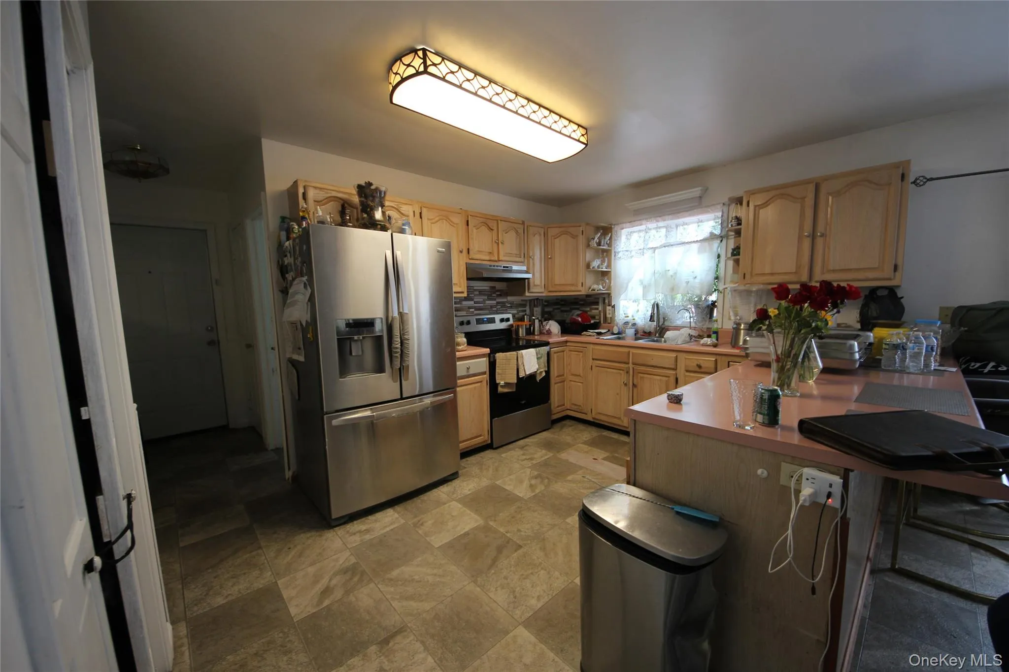 Kitchen featuring wood cabinetry, stainless steel appliances, a bar-height countertop, and patterned floor tiling Kitchen featuring wood cabinetry, stainless steel appliances, a bar-height countertop, and patterned floor tiling