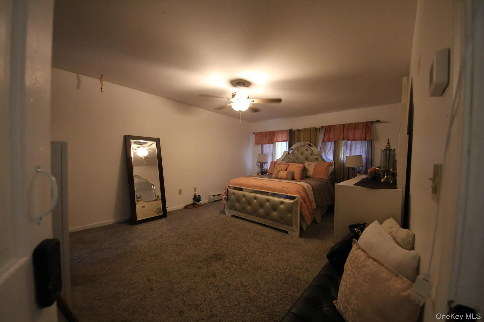 Carpeted interior room featuring a ceiling fan with light fixture, multiple windows with valances, and a built-in wall-mounted thermostat Carpeted interior room featuring a ceiling fan with light fixture, multiple windows with valances, and a built-in wall-mounted thermostat
