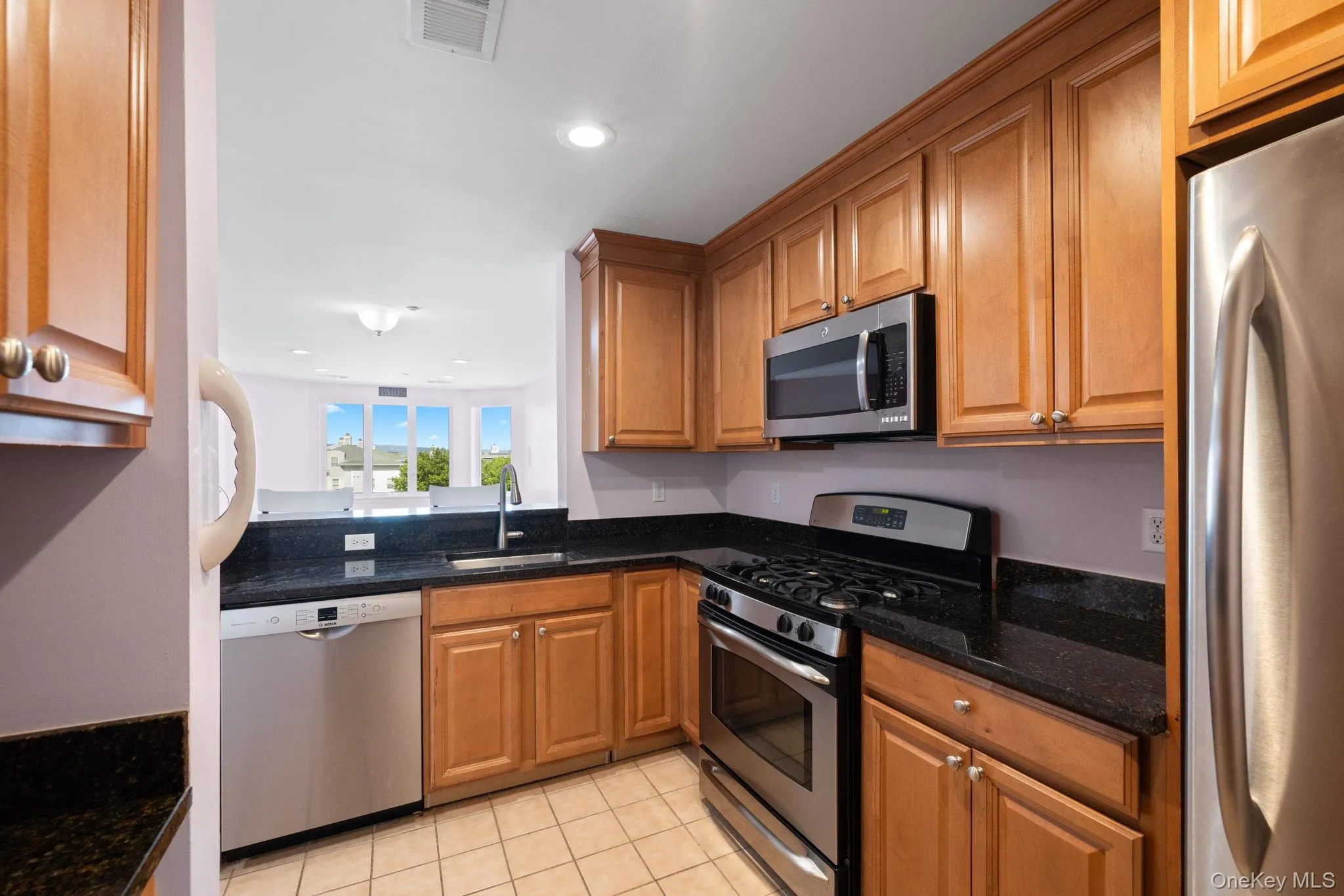 Kitchen featuring stainless steel appliances, dark countertops, wood cabinetry, and tile flooring Kitchen featuring stainless steel appliances, dark countertops, wood cabinetry, and tile flooring