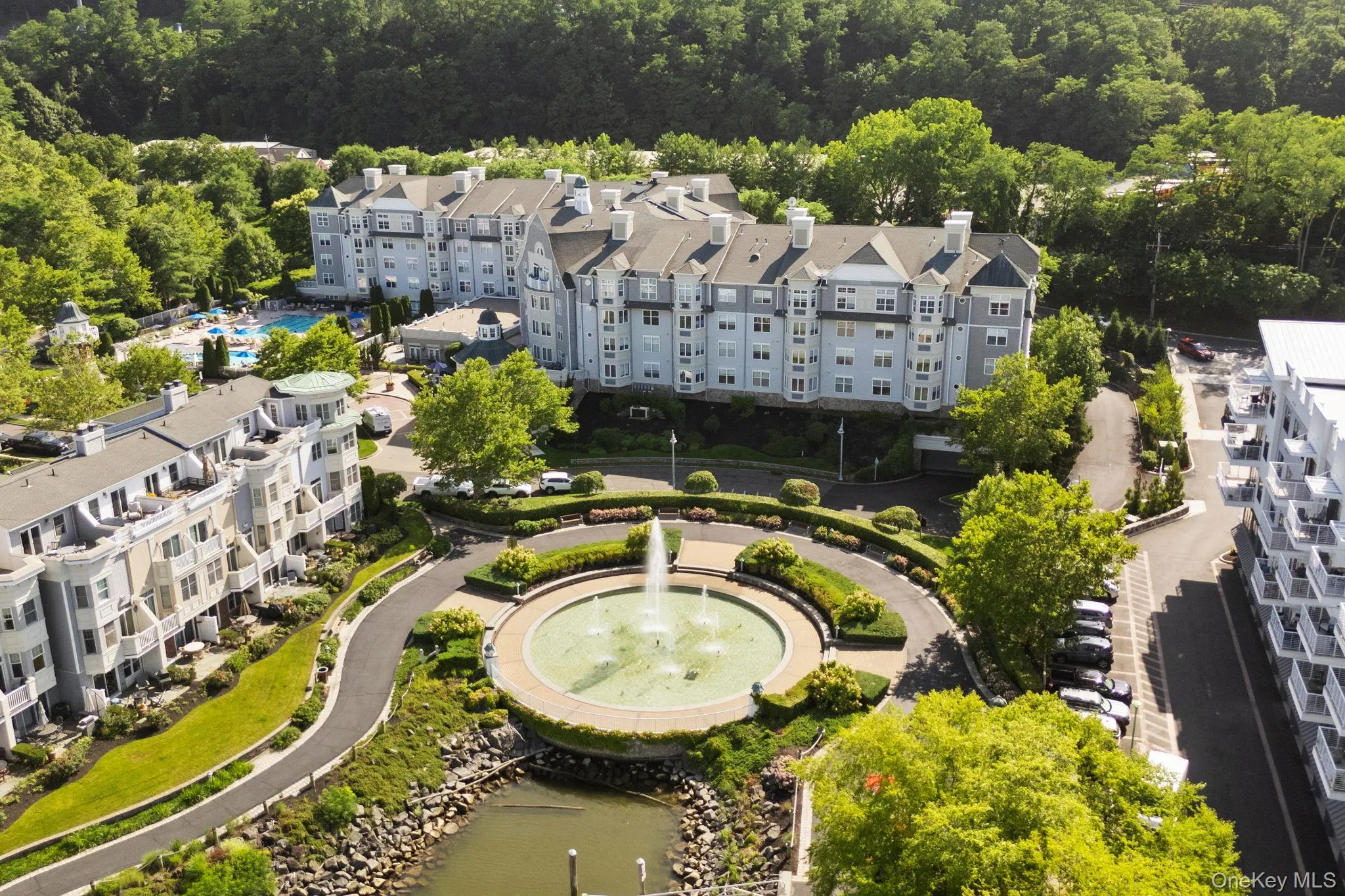 Central fountain feature surrounded by manicured landscaping, multi-story buildings with varied architectural styles, and an outdoor swimming pool area Central fountain feature surrounded by manicured landscaping, multi-story buildings with varied architectural styles, and an outdoor swimming pool area