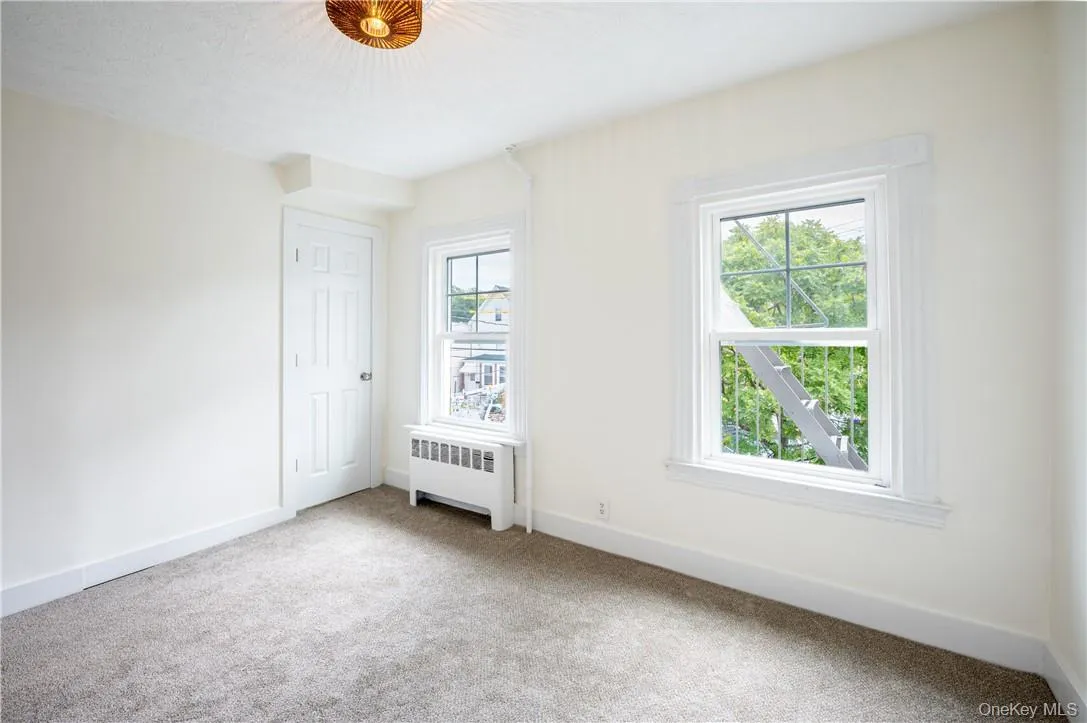 Another view of bedroom 1 with light colored carpet, radiator, and multiple windows Another view of bedroom 1 with light colored carpet, radiator, and multiple windows