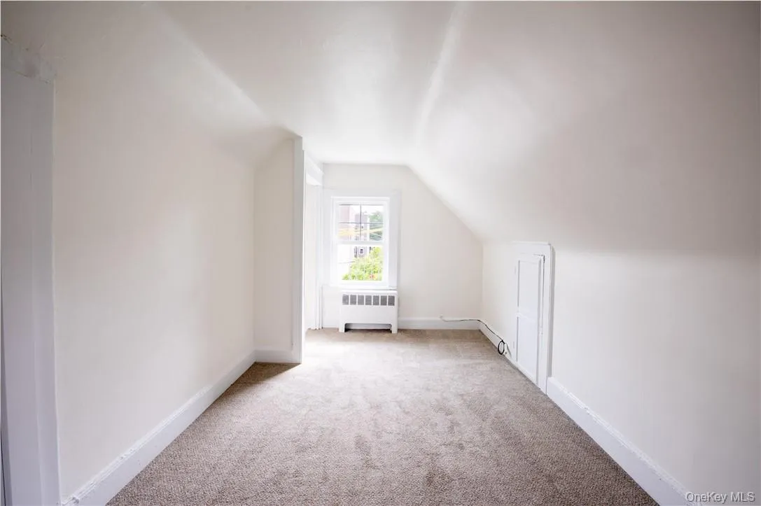Bedroom 2 on third floor featuring baseboard heating, vaulted ceiling, radiator, and light carpet Bedroom 2 on third floor featuring baseboard heating, vaulted ceiling, radiator, and light carpet