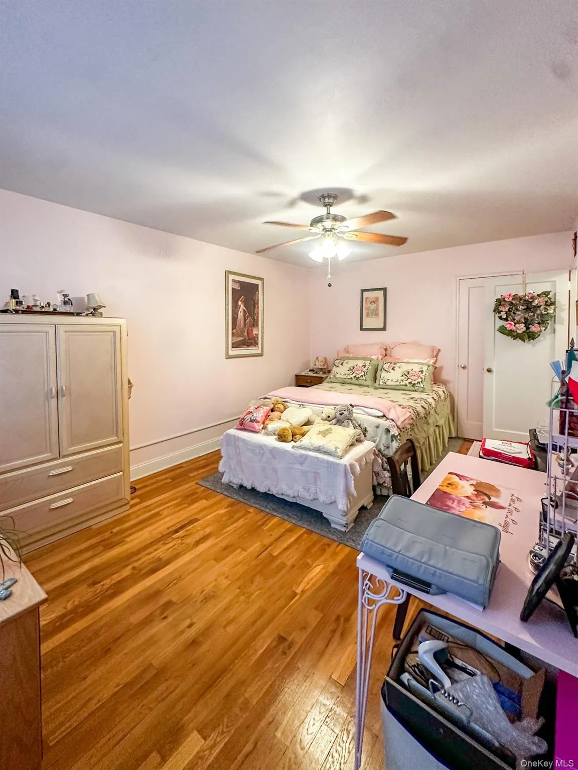 Warm bedroom space featuring wood-finish flooring, light-toned walls, and a ceiling fan with integrated lighting Warm bedroom space featuring wood-finish flooring, light-toned walls, and a ceiling fan with integrated lighting