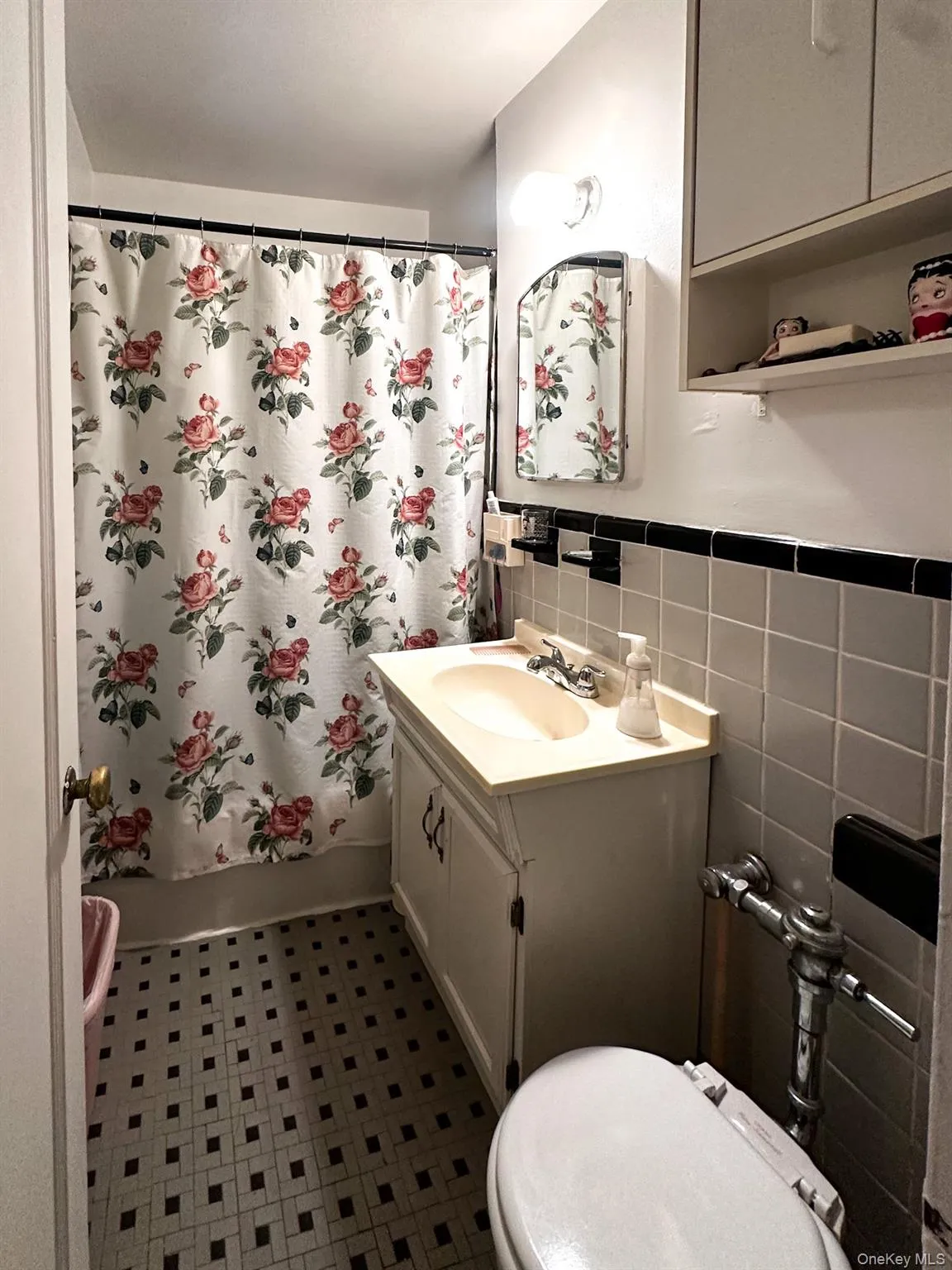 Bathroom featuring a vanity with an integrated sink, coordinating wall cabinets, black and white mosaic tile flooring, and a tiled shower surround Bathroom featuring a vanity with an integrated sink, coordinating wall cabinets, black and white mosaic tile flooring, and a tiled shower surround