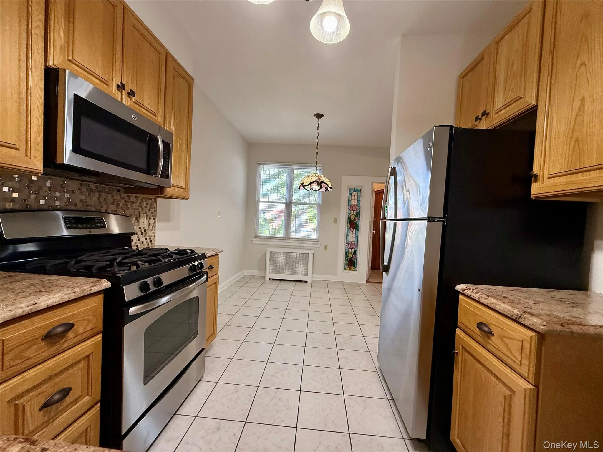 Kitchen featuring light wood cabinetry, stainless steel appliances, and a mosaic tile backsplash Kitchen featuring light wood cabinetry, stainless steel appliances, and a mosaic tile backsplash