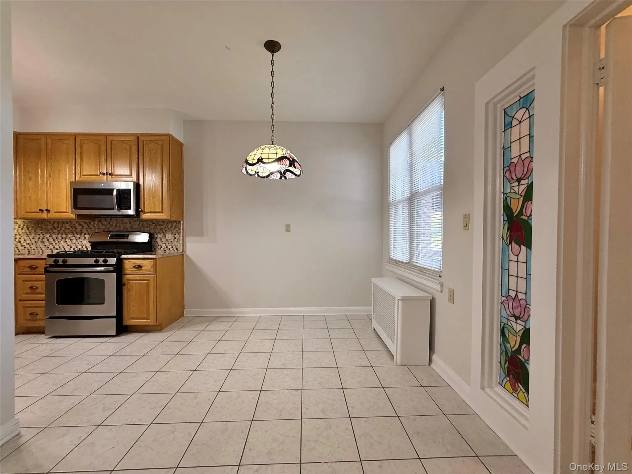 Dining area next to the kitchen space featuring tile flooring, oak wood finish cabinetry, stainless steel appliances, and a patterned tile backsplash Dining area next to the kitchen space featuring tile flooring, oak wood finish cabinetry, stainless steel appliances, and a patterned tile backsplash