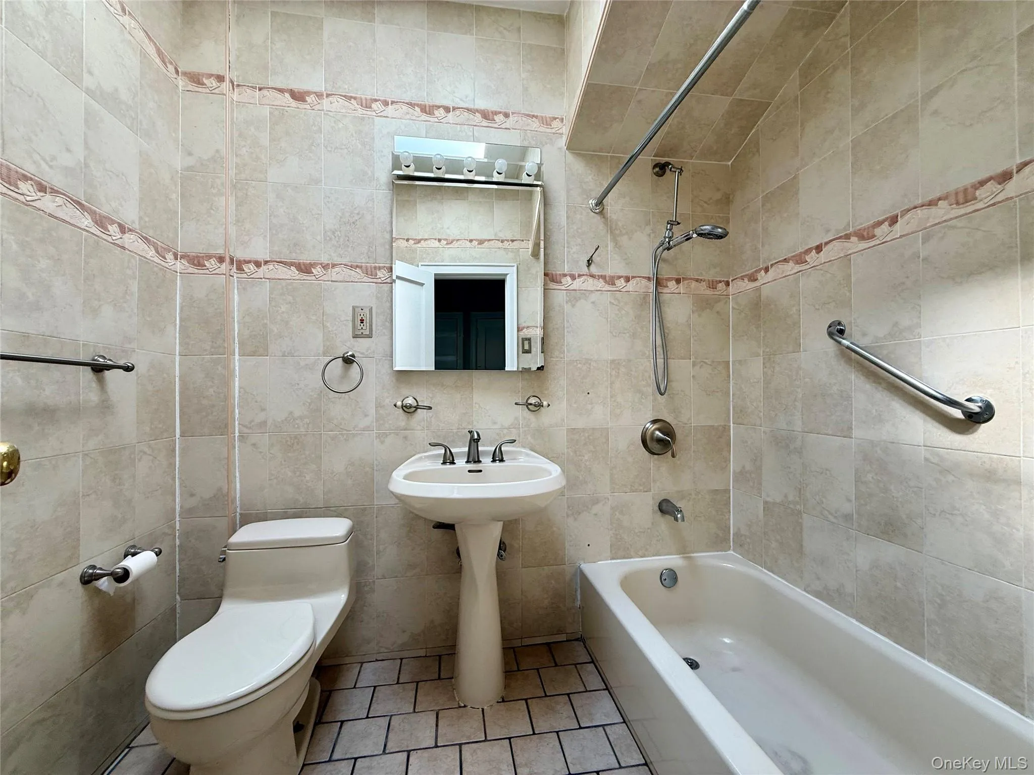 Bathroom featuring a pedestal sink, white bathtub, and floor to ceiling tiled walls and a skylight Bathroom featuring a pedestal sink, white bathtub, and floor to ceiling tiled walls and a skylight