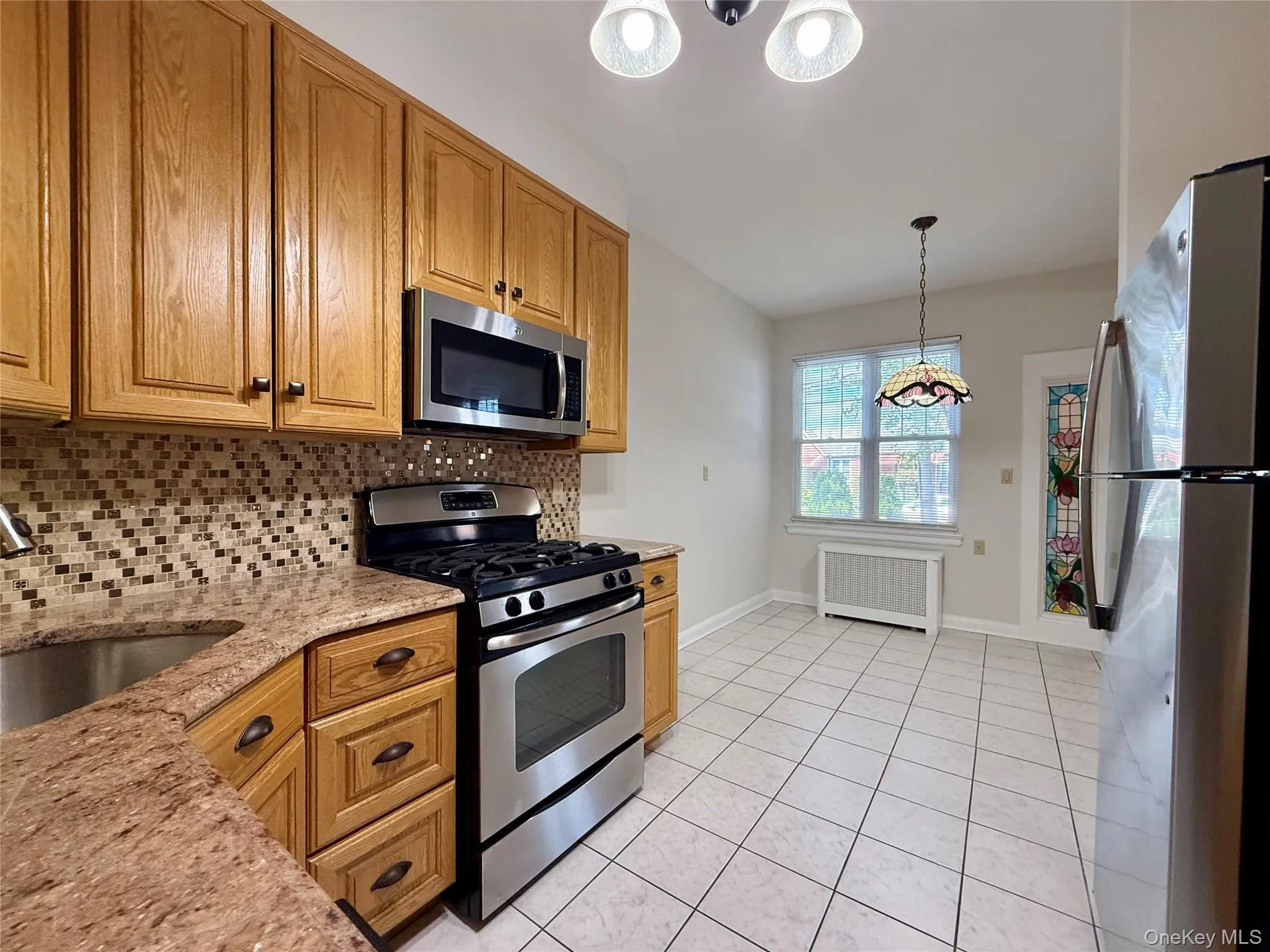Kitchen featuring wood cabinetry, stainless steel appliances, mosaic tile backsplash, and stone finish countertops Kitchen featuring wood cabinetry, stainless steel appliances, mosaic tile backsplash, and stone finish countertops