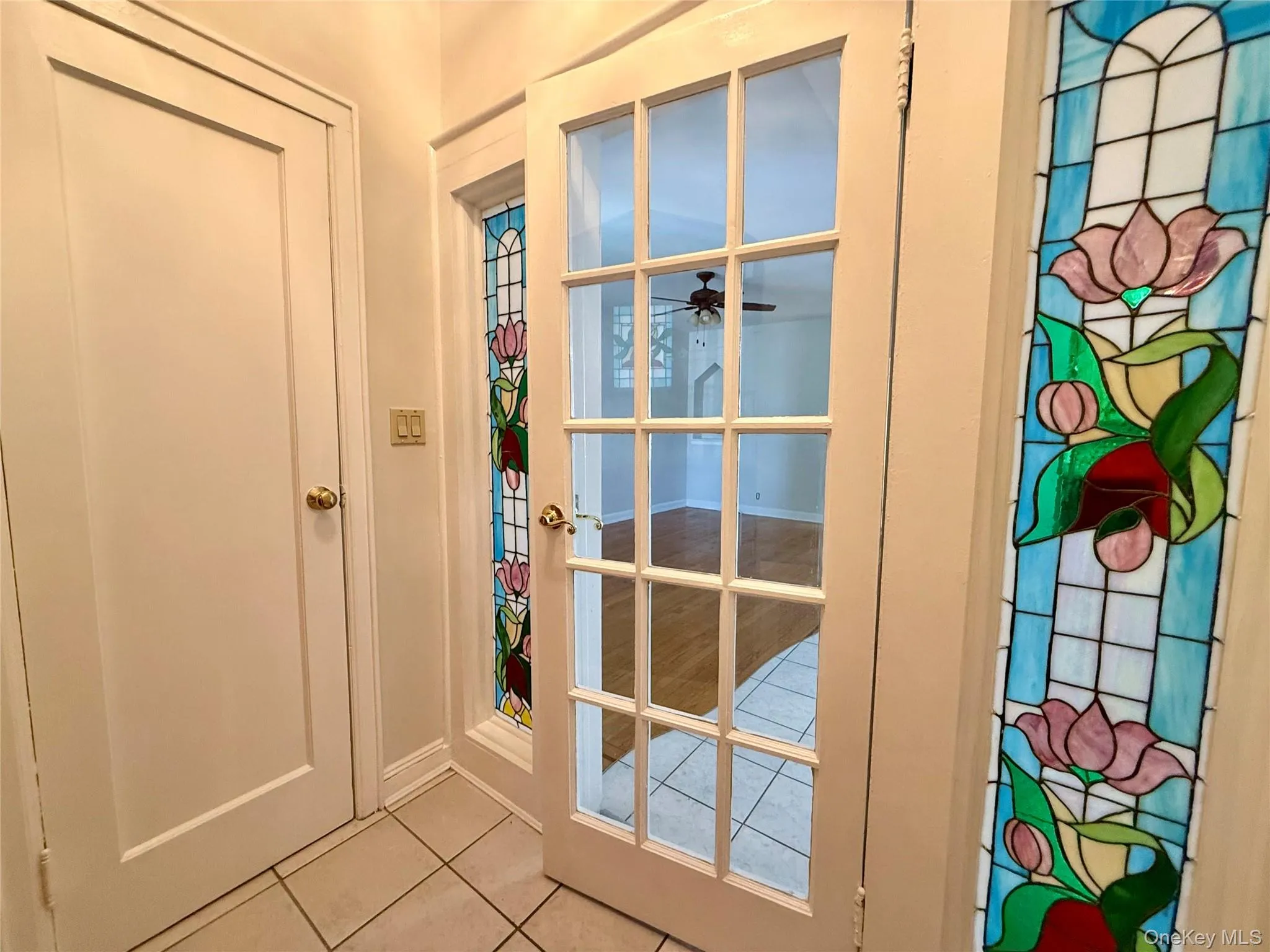 Entryway featuring ceramic tile flooring, a paneled door with brass hardware, and decorative stained glass window panels Entryway featuring ceramic tile flooring, a paneled door with brass hardware, and decorative stained glass window panels