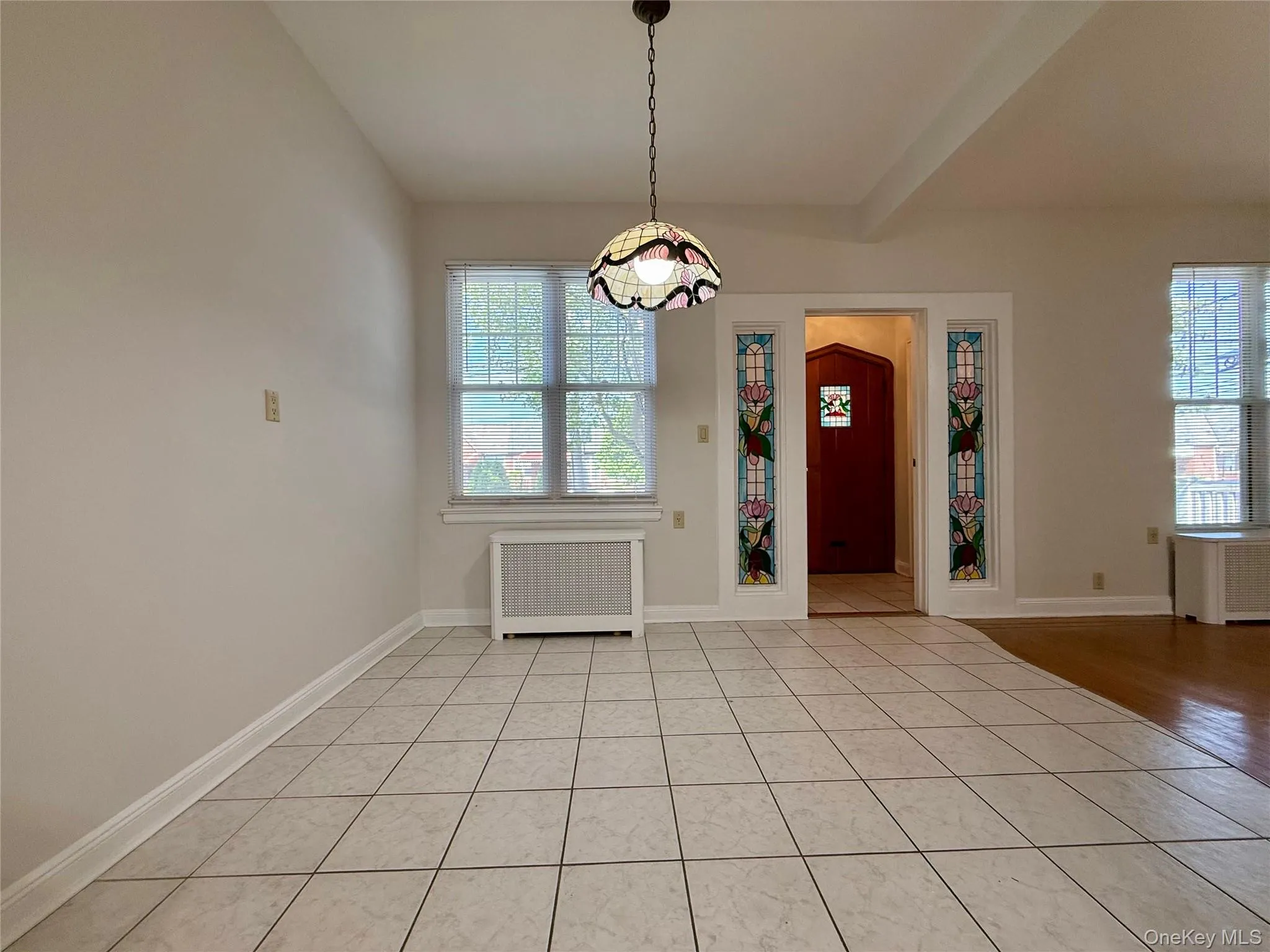 Spacious room featuring light toned tile flooring and a decorative stained glass chandelier Spacious room featuring light toned tile flooring and a decorative stained glass chandelier