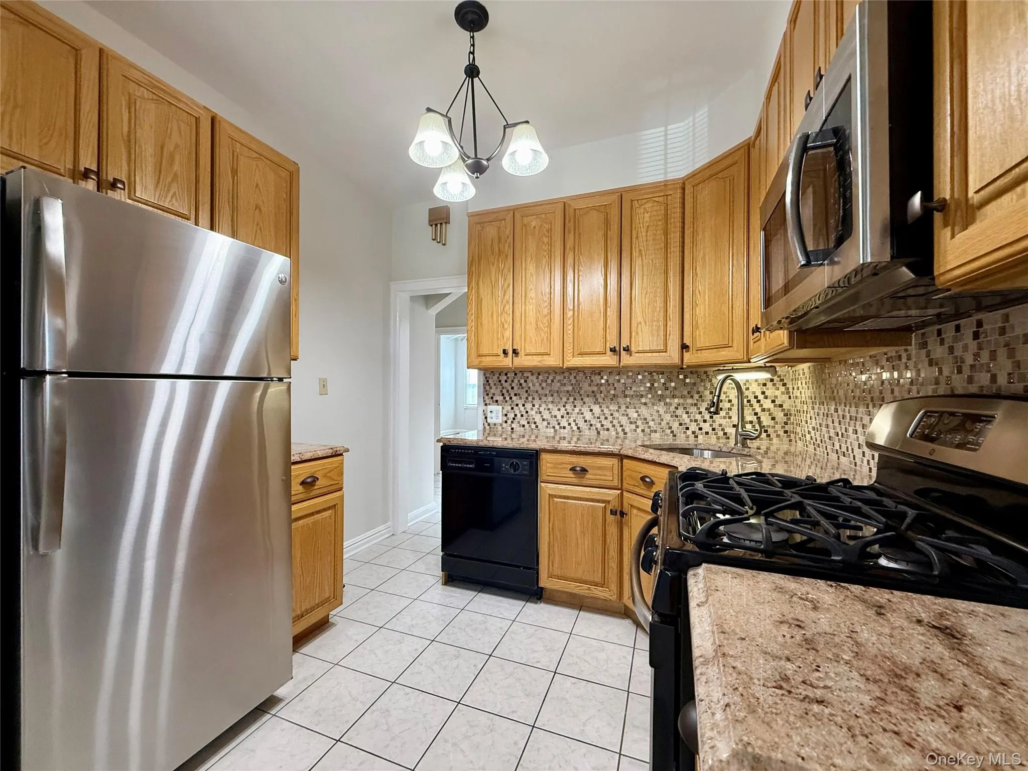 Kitchen featuring wood cabinetry, stainless steel appliances, speckled countertops, a mosaic tile backsplash, and white tile flooring Kitchen featuring wood cabinetry, stainless steel appliances, speckled countertops, a mosaic tile backsplash, and white tile flooring