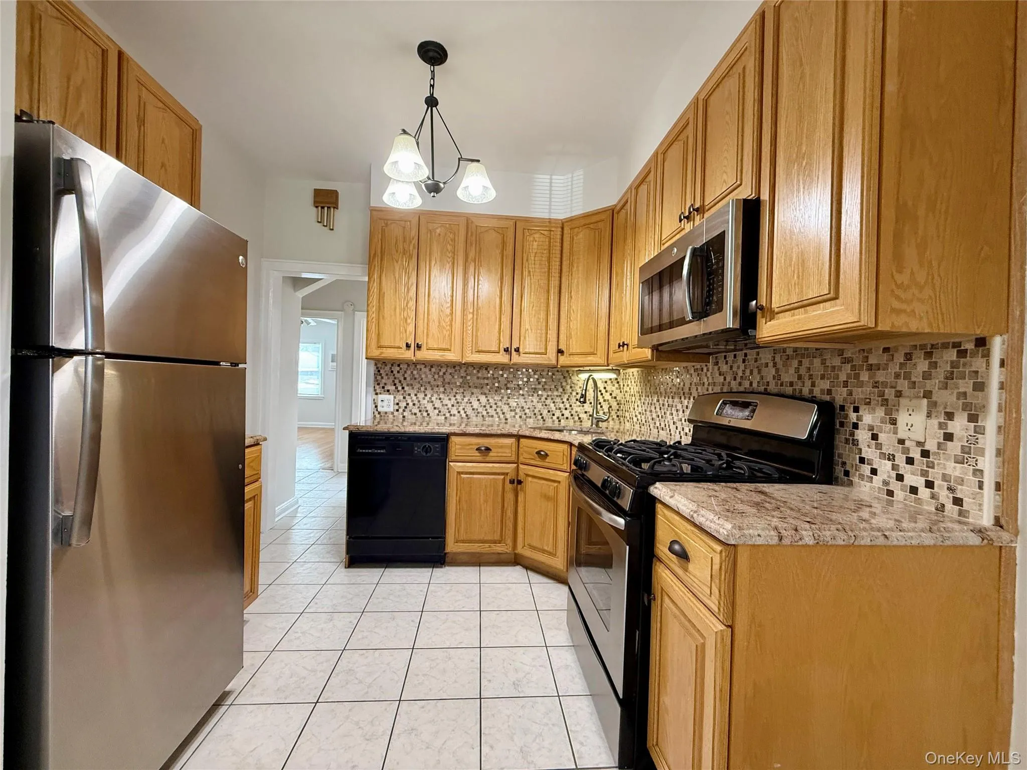 Kitchen featuring stainless steel appliances, oak finish cabinetry, tile flooring, mosaic tile backsplash, and a corner sink Kitchen featuring stainless steel appliances, oak finish cabinetry, tile flooring, mosaic tile backsplash, and a corner sink