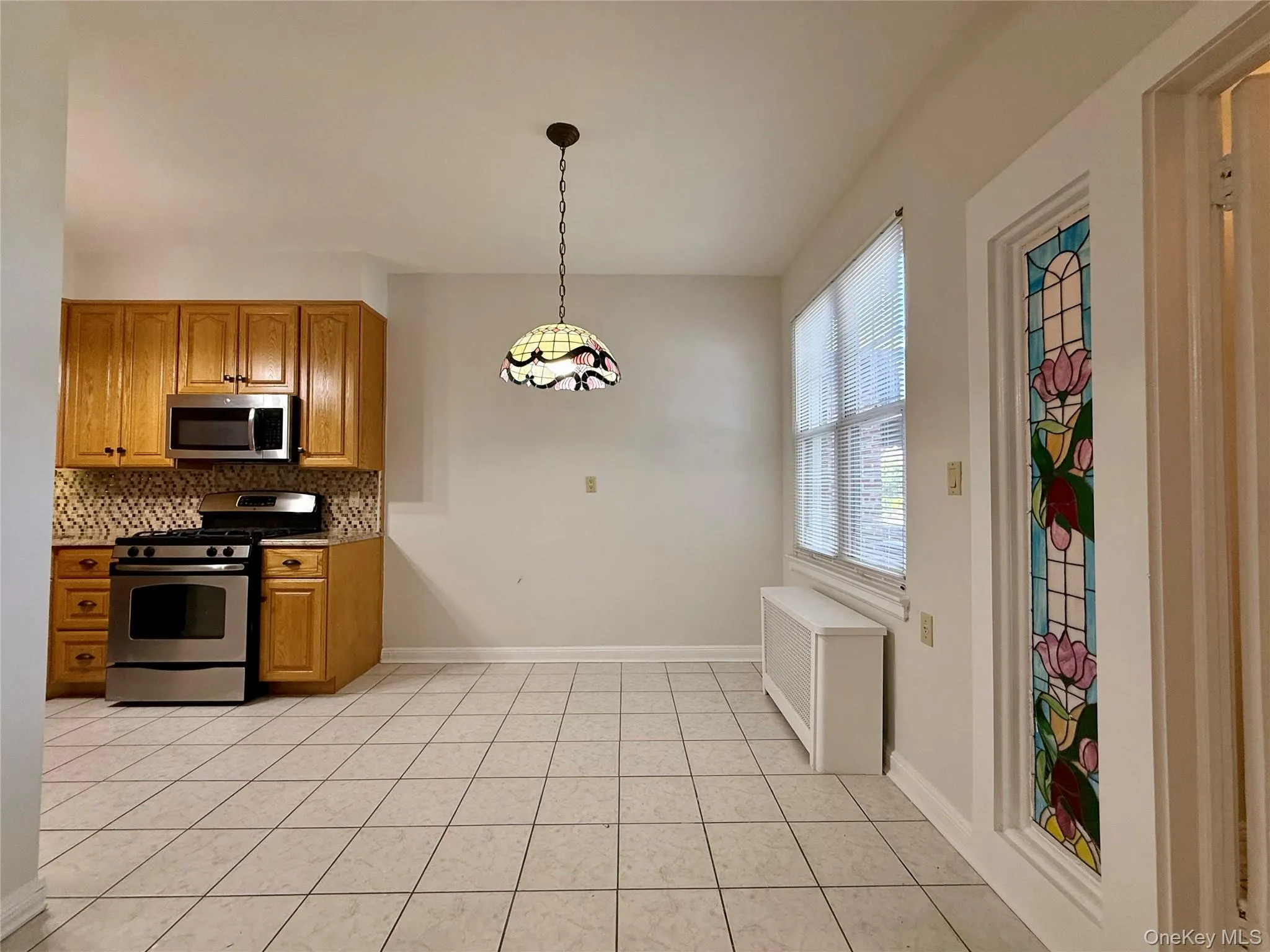 Dining area next to the kitchen space featuring tile flooring, oak wood finish cabinetry, stainless steel appliances, and a patterned tile backsplash Dining area next to the kitchen space featuring tile flooring, oak wood finish cabinetry, stainless steel appliances, and a patterned tile backsplash