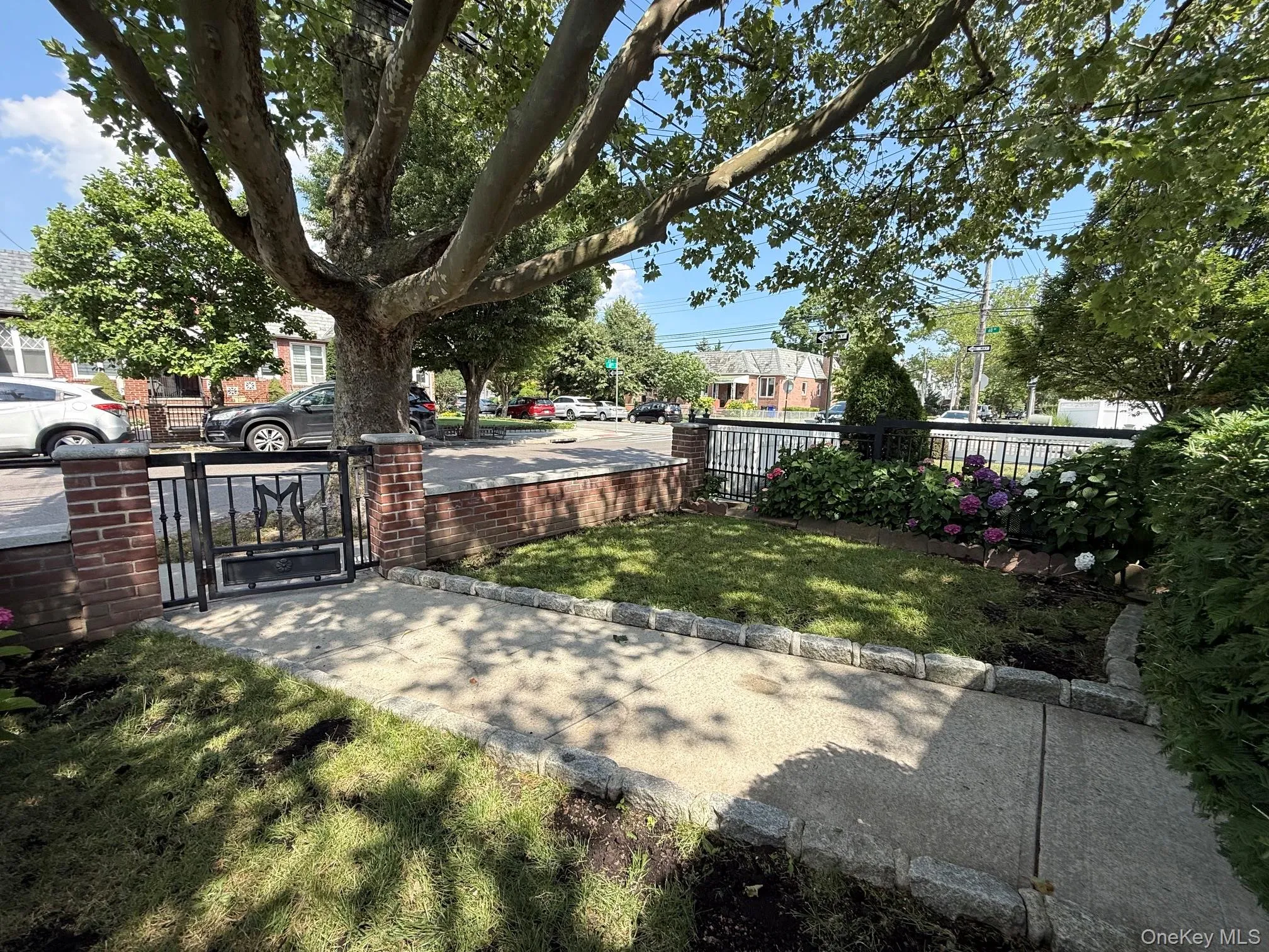Front yard featuring manicured lawn, brick and wrought iron fencing, mature tree, and planted garden beds Front yard featuring manicured lawn, brick and wrought iron fencing, mature tree, and planted garden beds