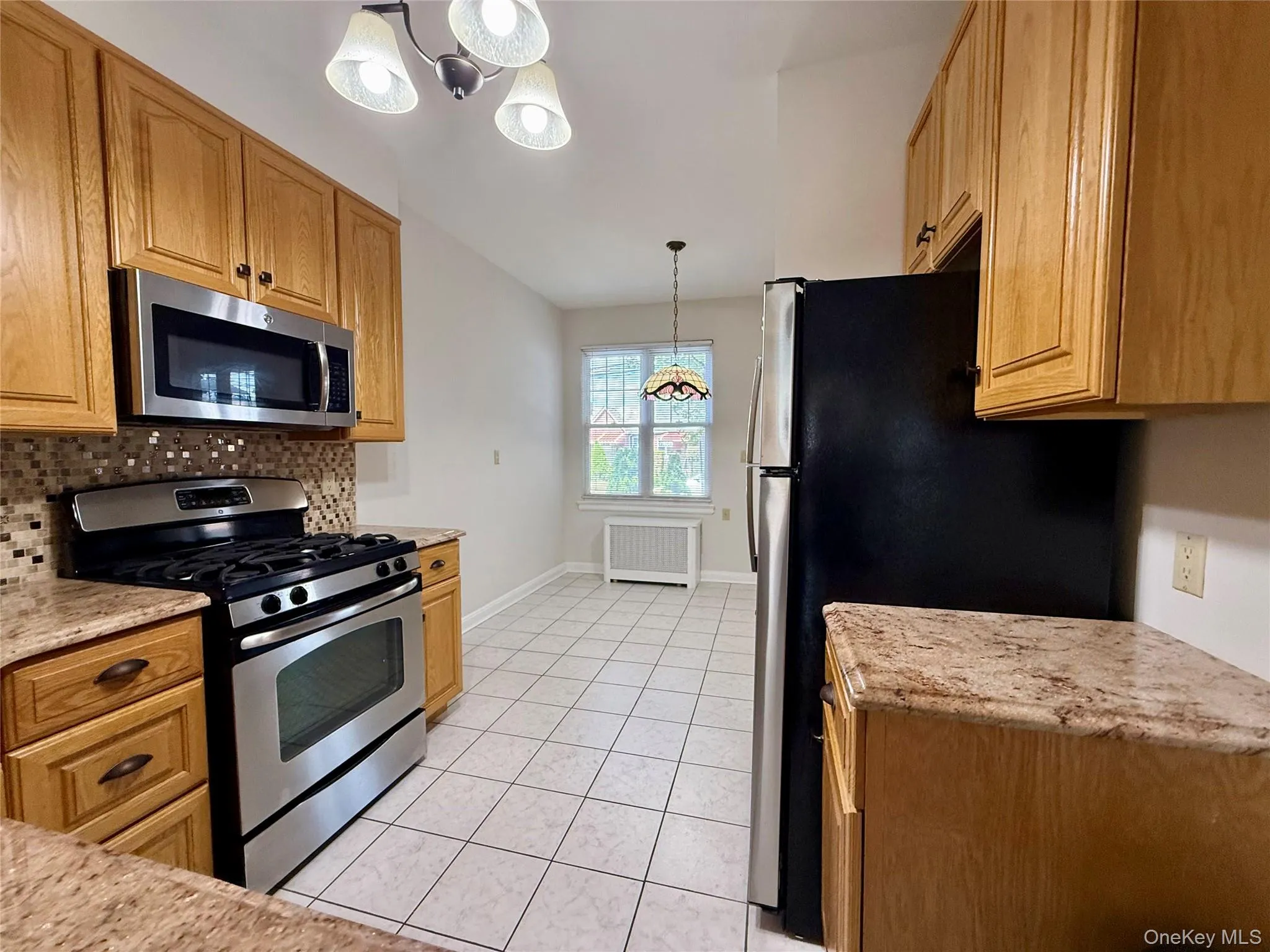 Kitchen featuring oak finish cabinetry, granite look countertops, and stainless steel appliances including a gas range and microwave Kitchen featuring oak finish cabinetry, granite look countertops, and stainless steel appliances including a gas range and microwave