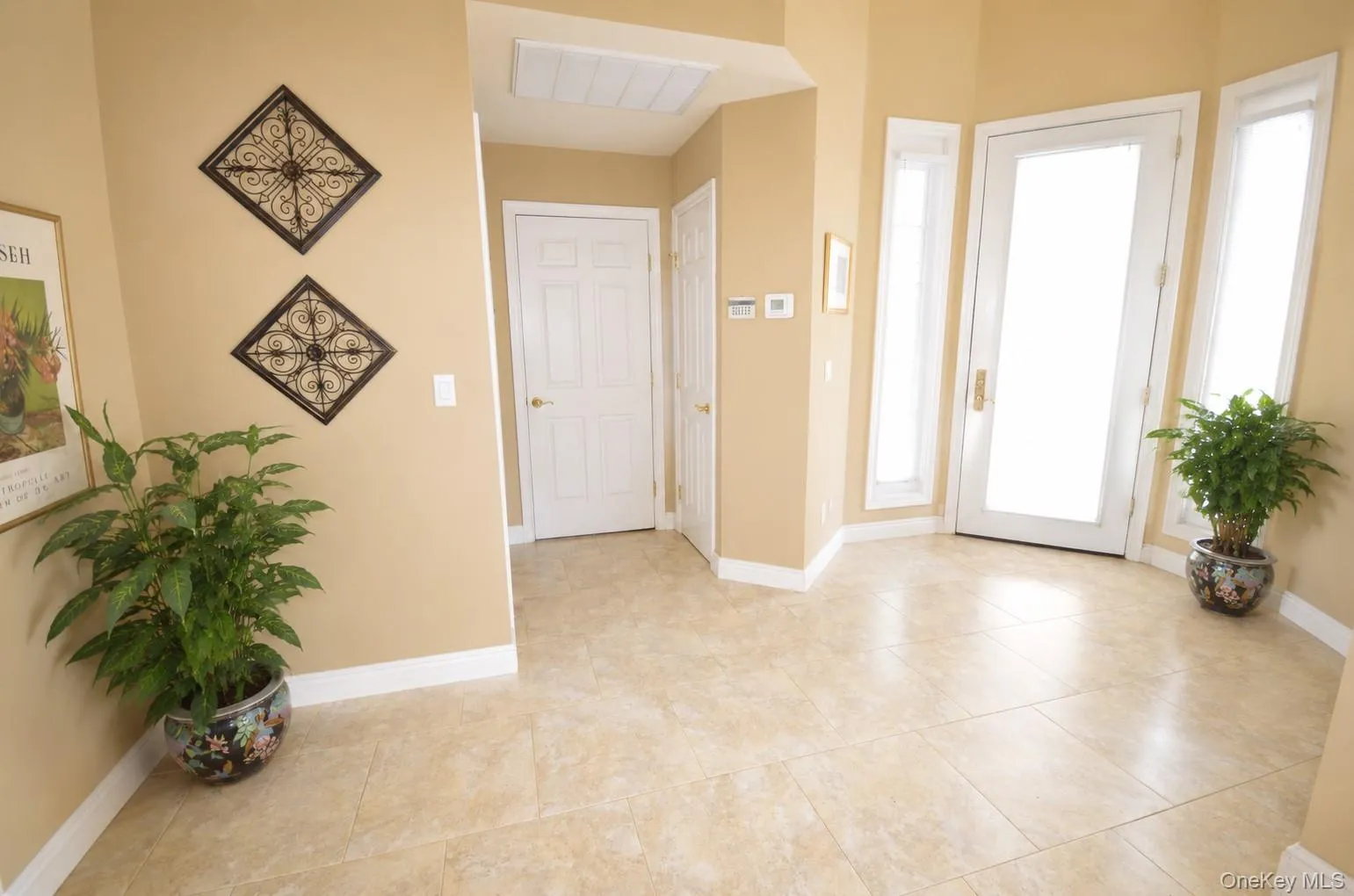 Tile flooring in a neutral tone with white baseboards, featuring a light-colored main entry door and two side light panels Tile flooring in a neutral tone with white baseboards, featuring a light-colored main entry door and two side light panels