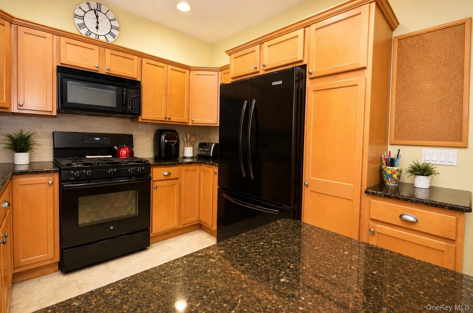 Spacious kitchen featuring wood cabinetry, black appliances, dark speckled countertops, tile backsplash, and recessed lighting Spacious kitchen featuring wood cabinetry, black appliances, dark speckled countertops, tile backsplash, and recessed lighting