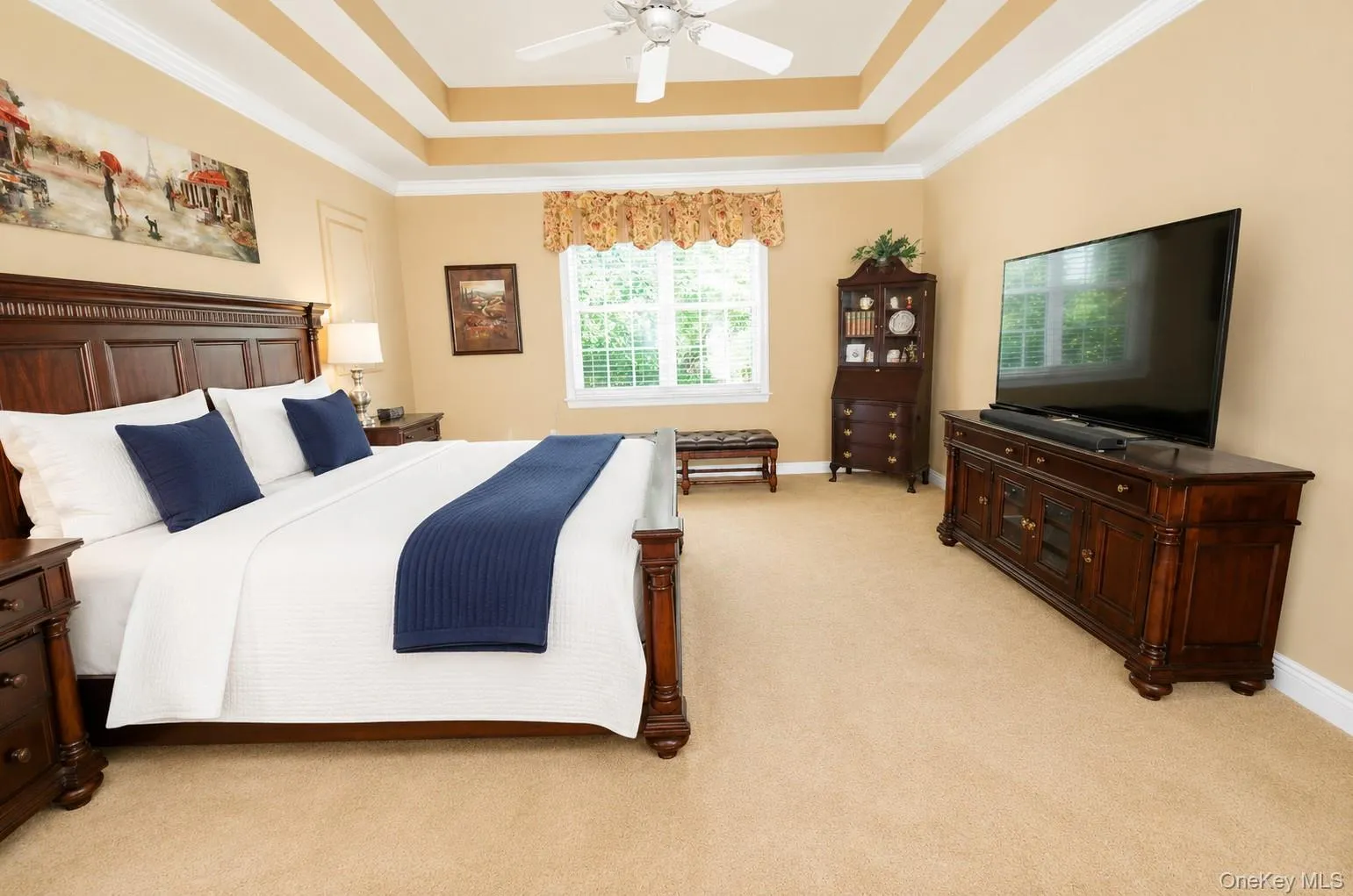 Expansive bedroom featuring a tray ceiling with a ceiling fan, plush carpeting, a large window with blinds, and built-in cabinetry Expansive bedroom featuring a tray ceiling with a ceiling fan, plush carpeting, a large window with blinds, and built-in cabinetry