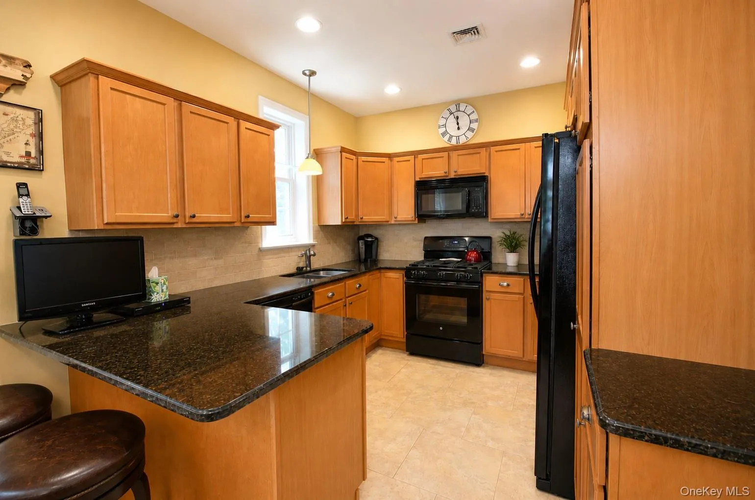 Kitchen featuring wood cabinetry, dark granite-style countertops, black appliances, and a tile backsplash Kitchen featuring wood cabinetry, dark granite-style countertops, black appliances, and a tile backsplash