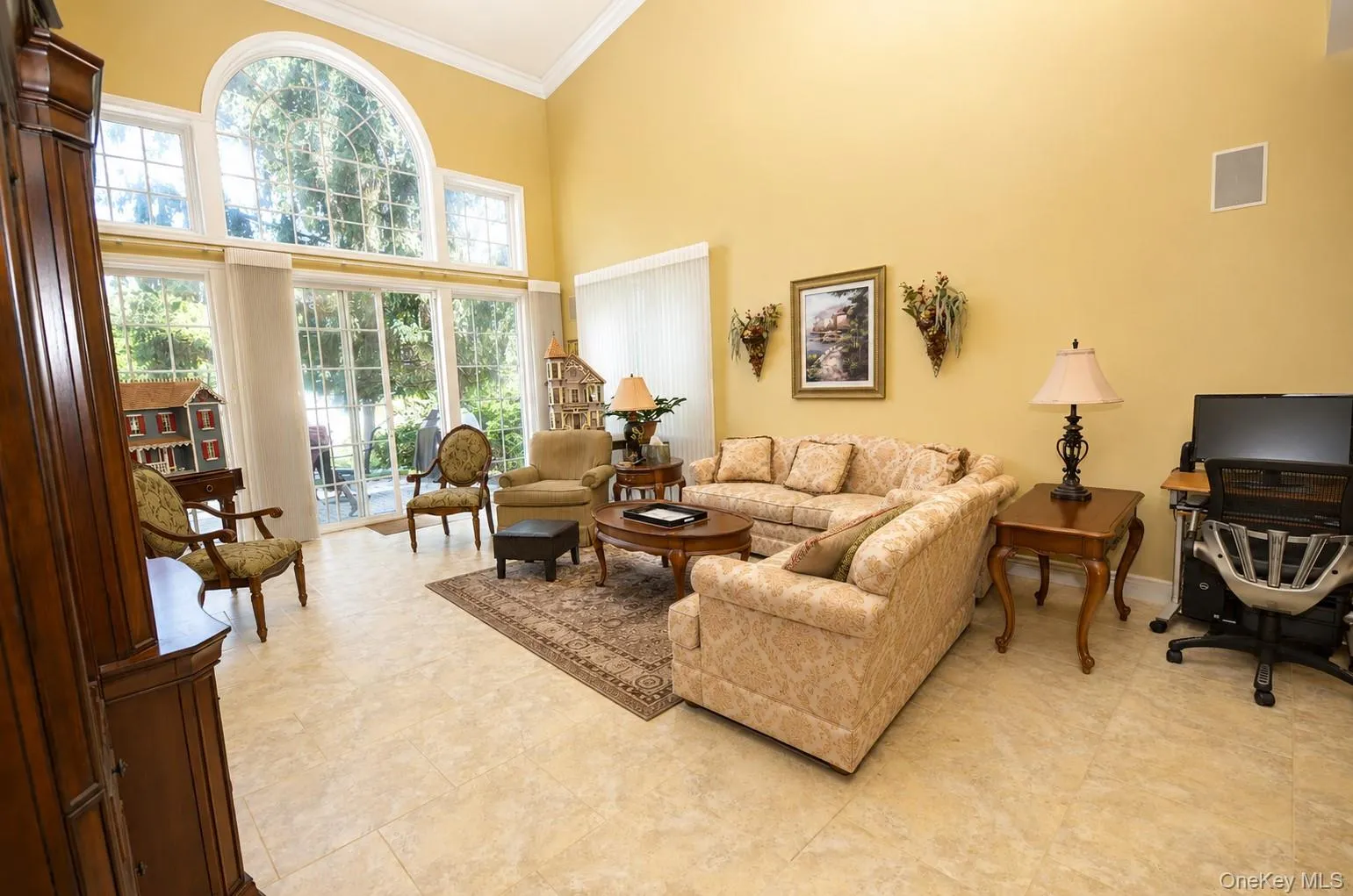 Spacious living area featuring high vaulted ceilings, expansive arched windows, sliding glass doors, and light-toned tile flooring Spacious living area featuring high vaulted ceilings, expansive arched windows, sliding glass doors, and light-toned tile flooring