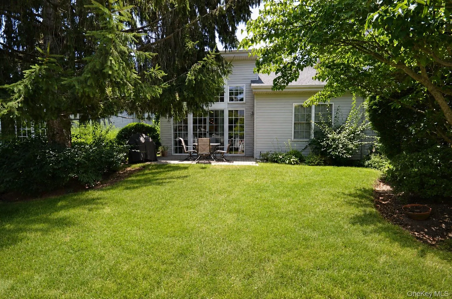 Spacious back featuring a manicured lawn, mature trees, and a paved patio area Spacious back featuring a manicured lawn, mature trees, and a paved patio area