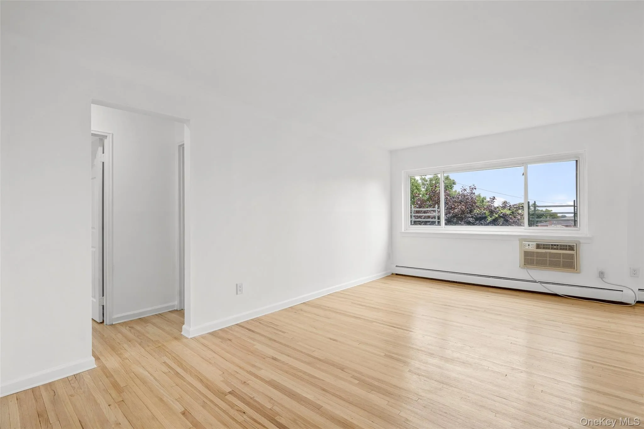 Living room with large windows overlooking the building grounds.In wall air conditioning unit. Living room with large windows overlooking the building grounds.In wall air conditioning unit.