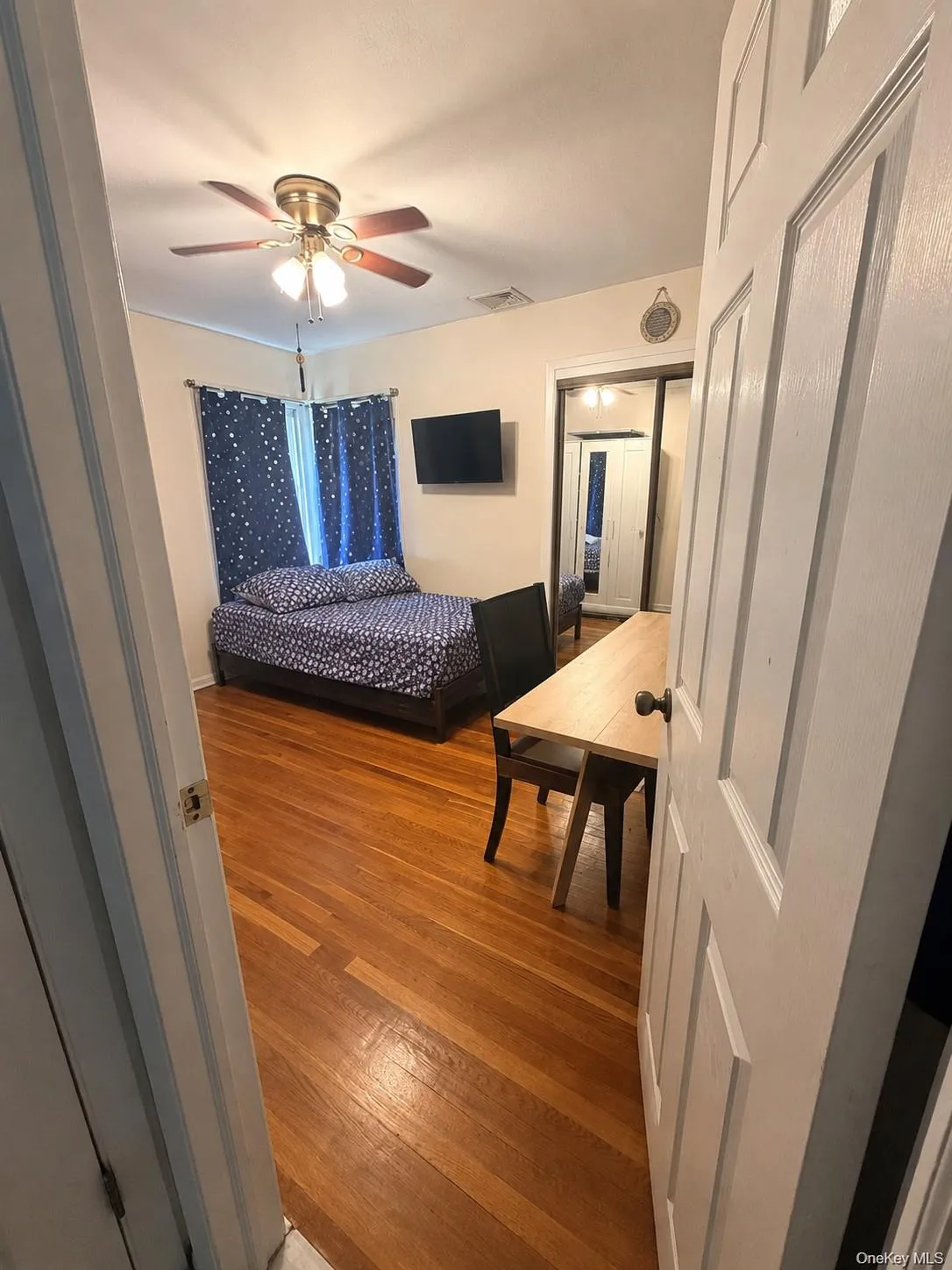 Room with wood-finish flooring, a ceiling fan with integrated lighting, and a mirrored closet Room with wood-finish flooring, a ceiling fan with integrated lighting, and a mirrored closet