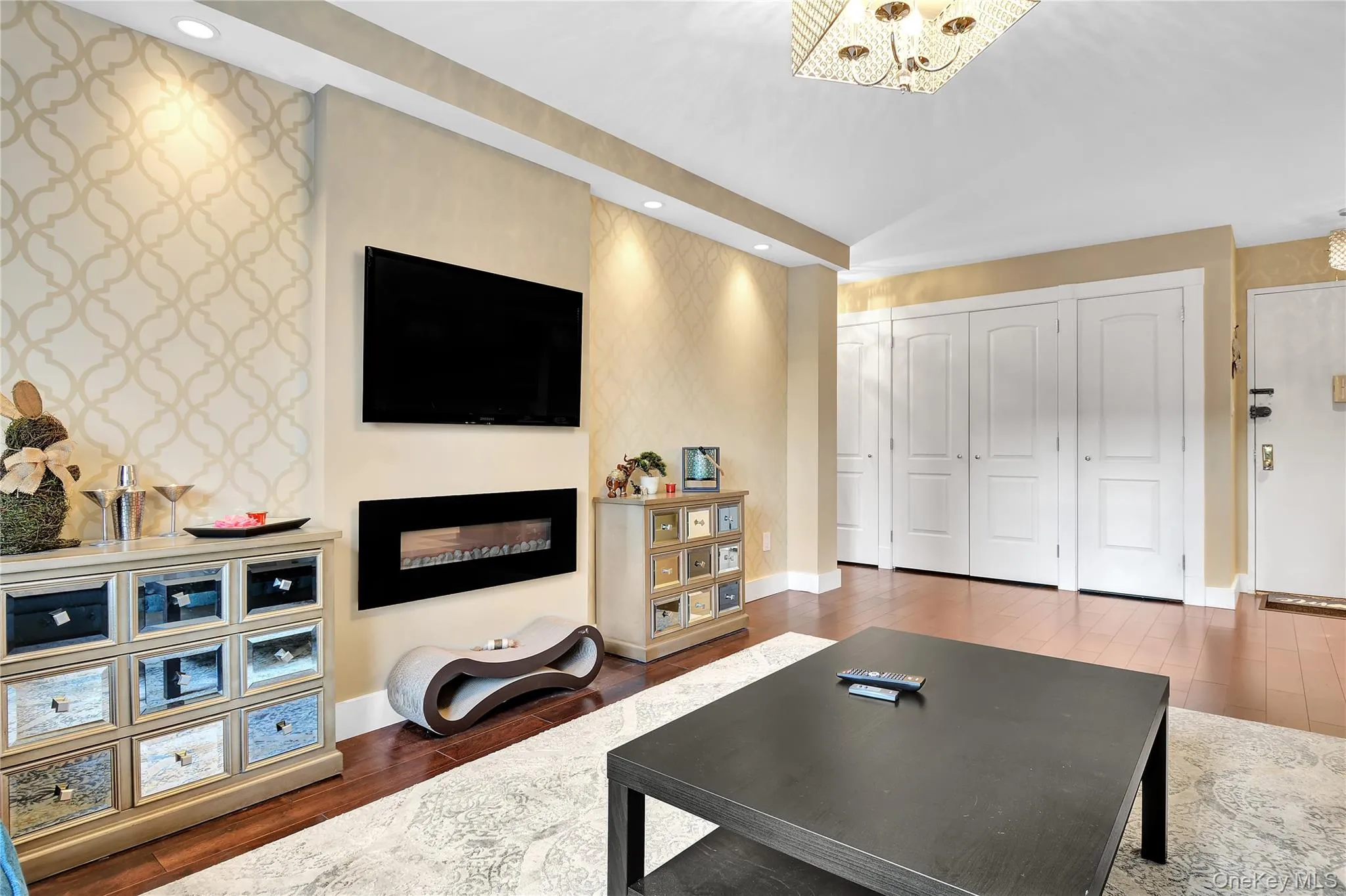 Living area featuring dark wood finished floors, a fireplace, wallpapered walls, recessed lighting, and an accent wall Living area featuring dark wood finished floors, a fireplace, wallpapered walls, recessed lighting, and an accent wall