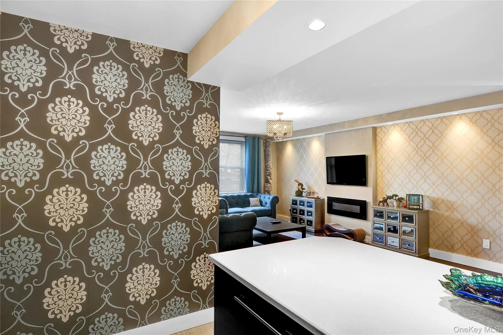 Kitchen featuring wallpapered walls, dark cabinetry, open floor plan, a chandelier, and hanging light fixtures Kitchen featuring wallpapered walls, dark cabinetry, open floor plan, a chandelier, and hanging light fixtures