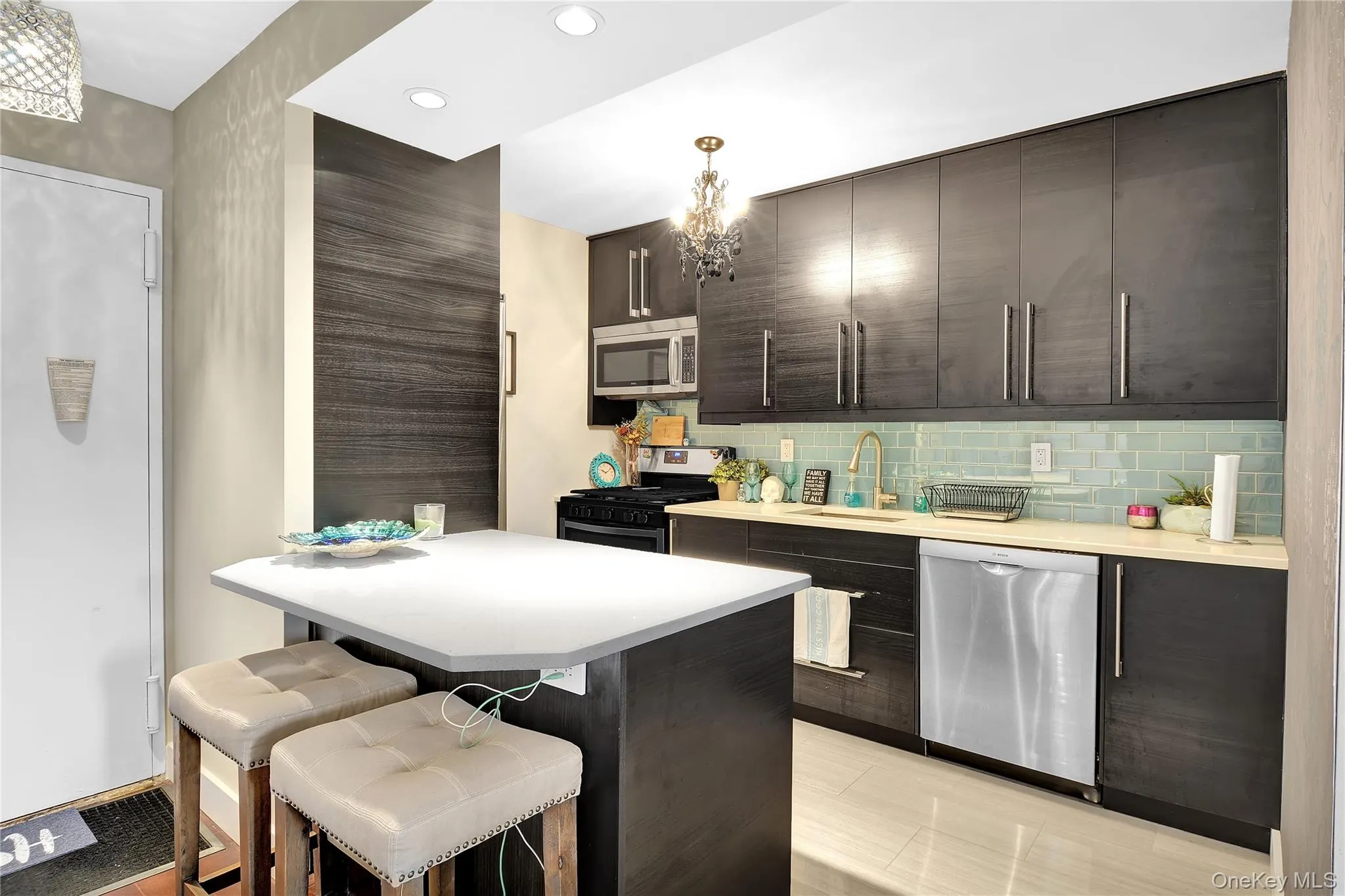 Kitchen with hanging light fixtures, stainless steel appliances, backsplash, a kitchen breakfast bar, and a chandelier Kitchen with hanging light fixtures, stainless steel appliances, backsplash, a kitchen breakfast bar, and a chandelier