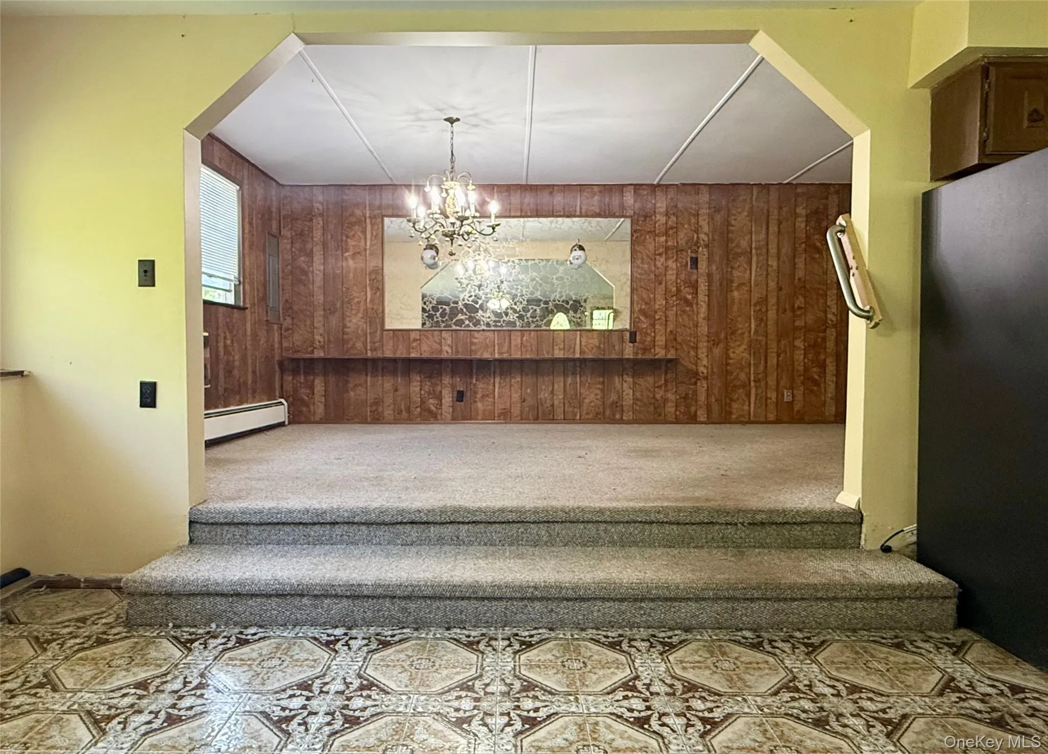 Staircase featuring a baseboard heating unit, carpet flooring, wooden walls, and a chandelier Staircase featuring a baseboard heating unit, carpet flooring, wooden walls, and a chandelier