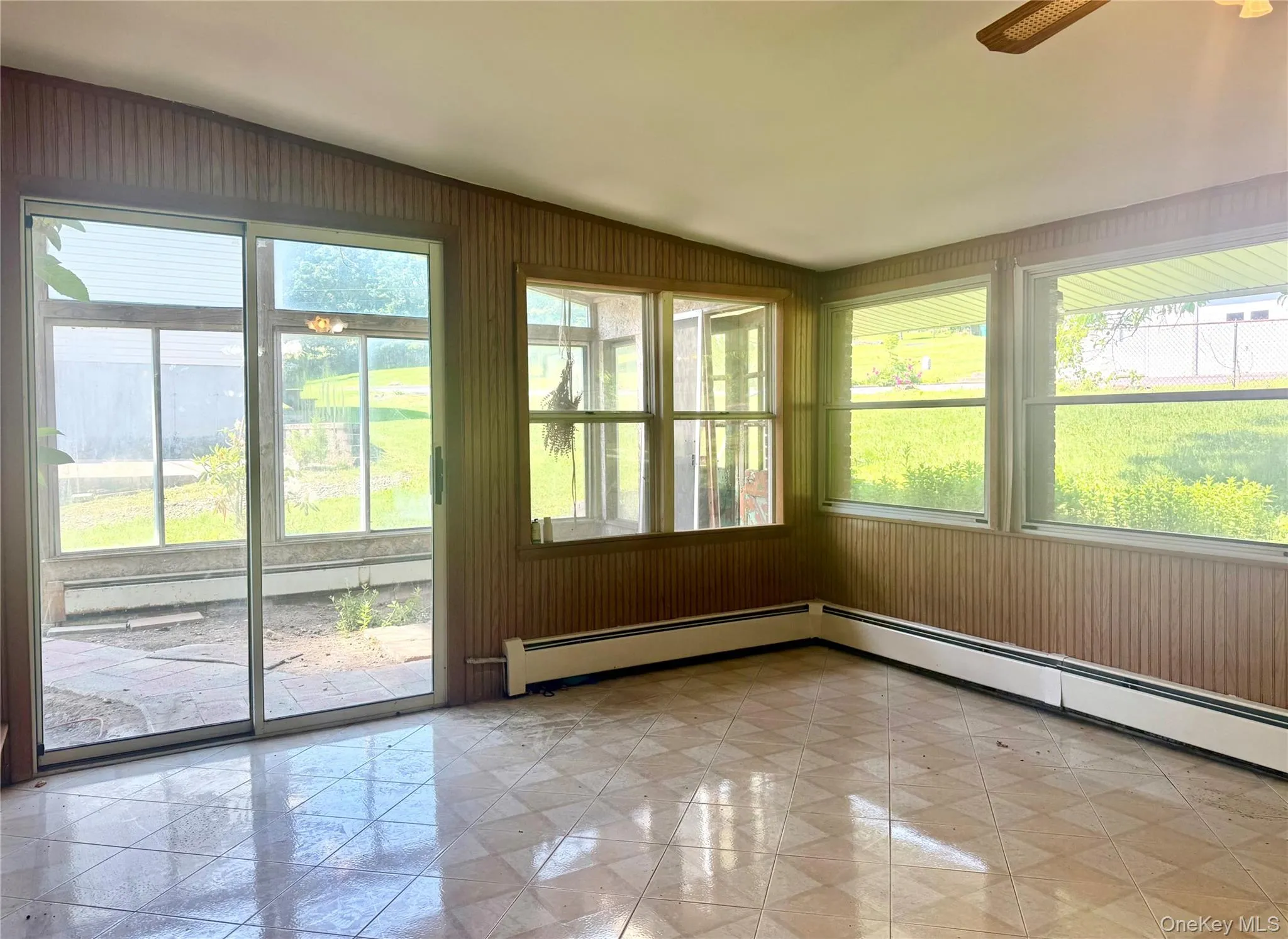 Unfurnished sunroom featuring healthy amount of natural light, baseboard heating, and wood walls Unfurnished sunroom featuring healthy amount of natural light, baseboard heating, and wood walls