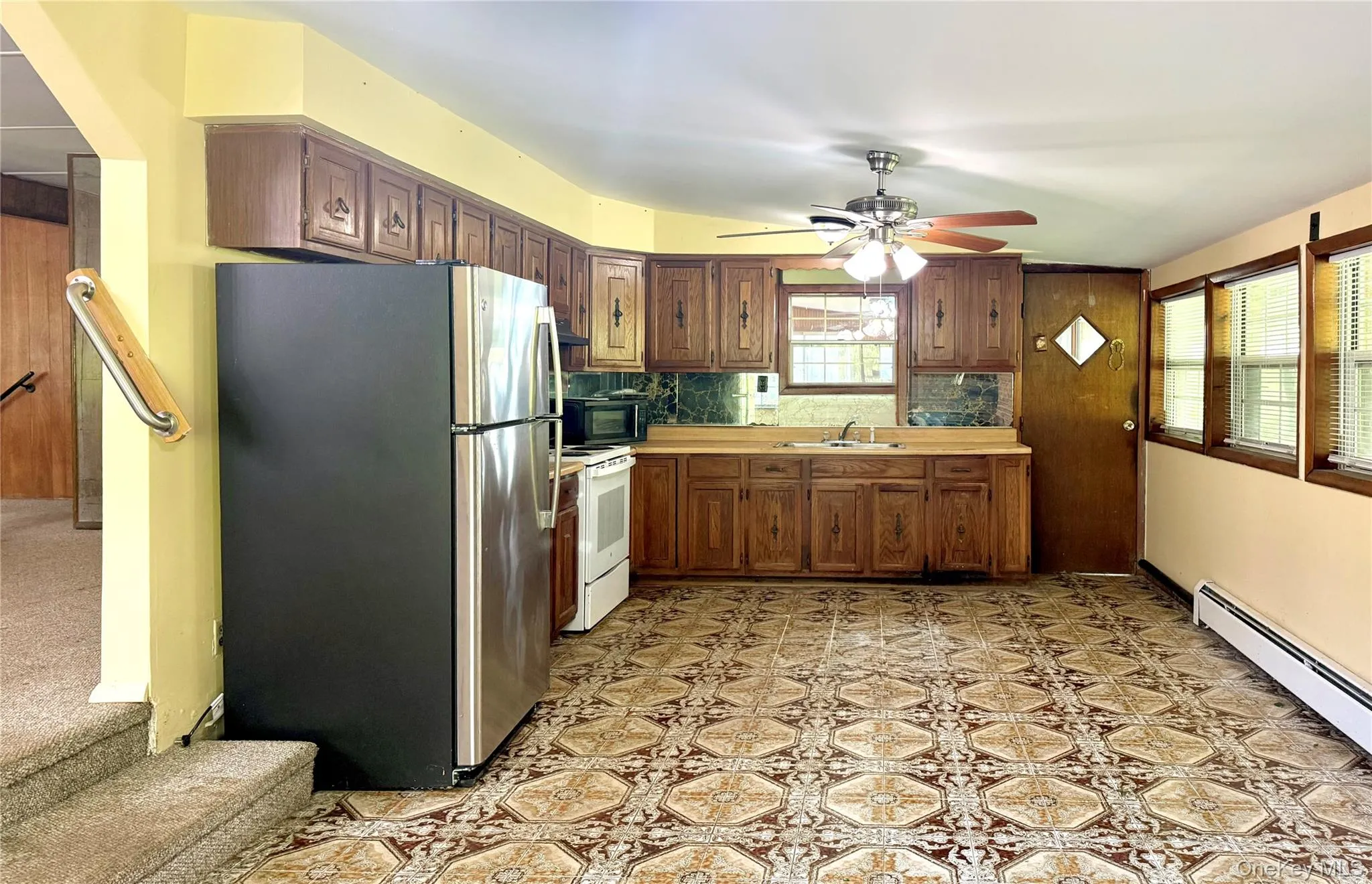 Kitchen with freestanding refrigerator, white range with electric cooktop, a sink, black microwave, and a baseboard radiator Kitchen with freestanding refrigerator, white range with electric cooktop, a sink, black microwave, and a baseboard radiator