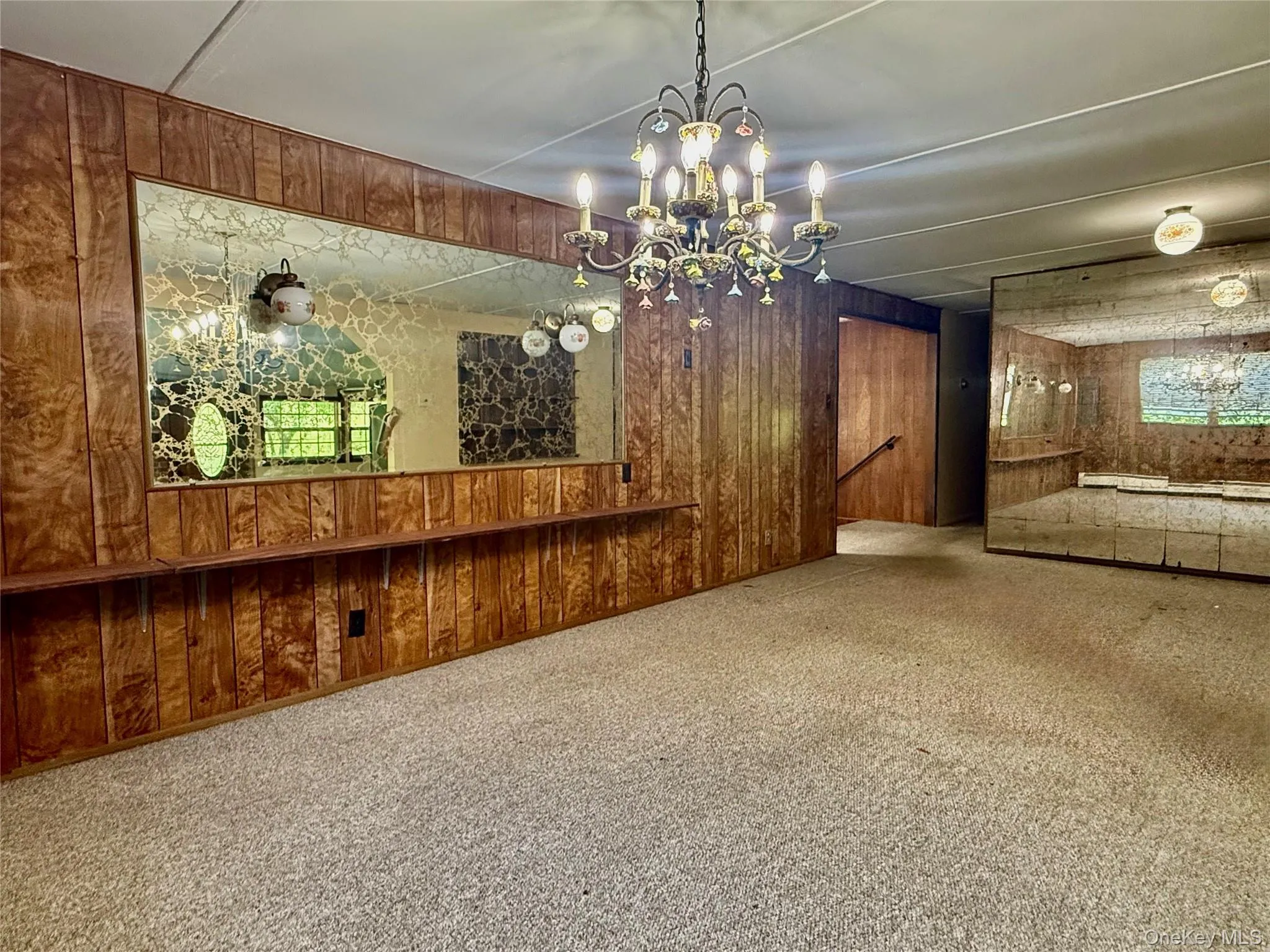 Unfurnished living room with wooden walls, a chandelier, and carpet Unfurnished living room with wooden walls, a chandelier, and carpet