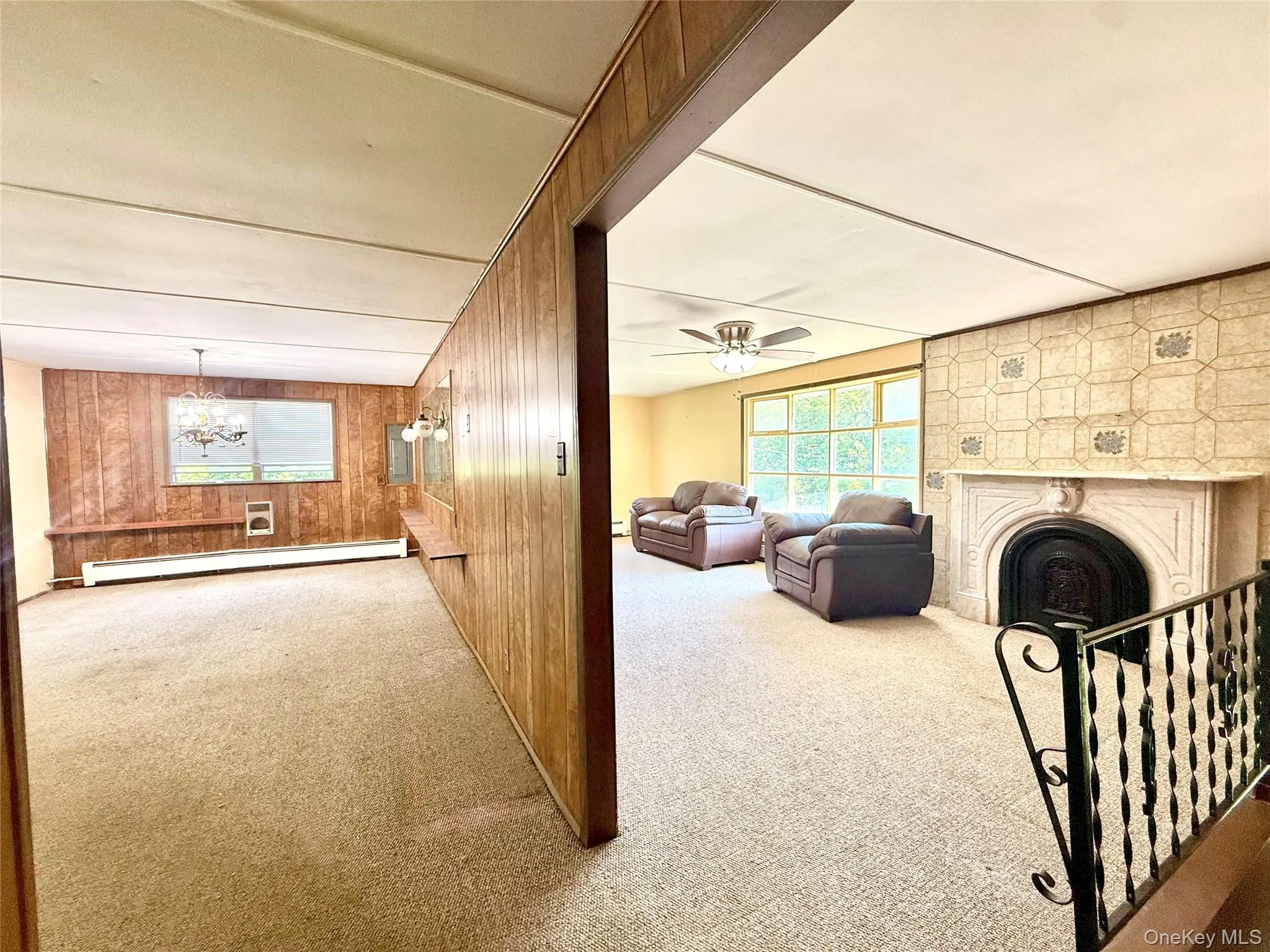 Living area featuring baseboard heating, carpet, wood walls, a fireplace, and ceiling fan Living area featuring baseboard heating, carpet, wood walls, a fireplace, and ceiling fan