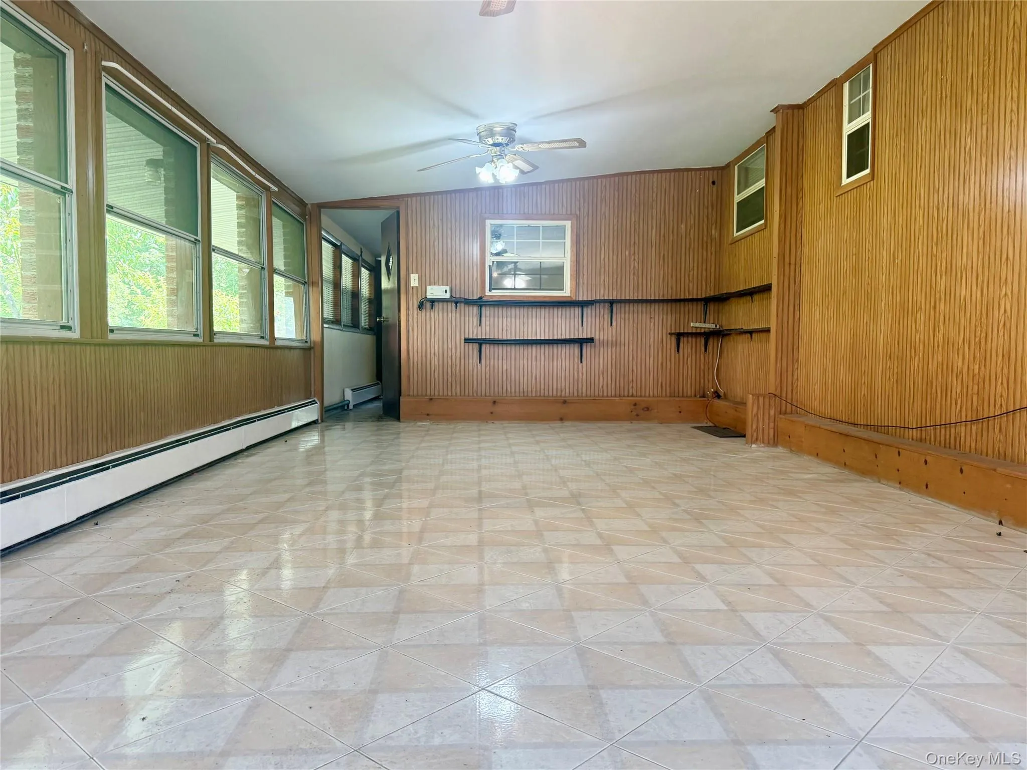 Empty room featuring ceiling fan, baseboard heating, and wood walls Empty room featuring ceiling fan, baseboard heating, and wood walls