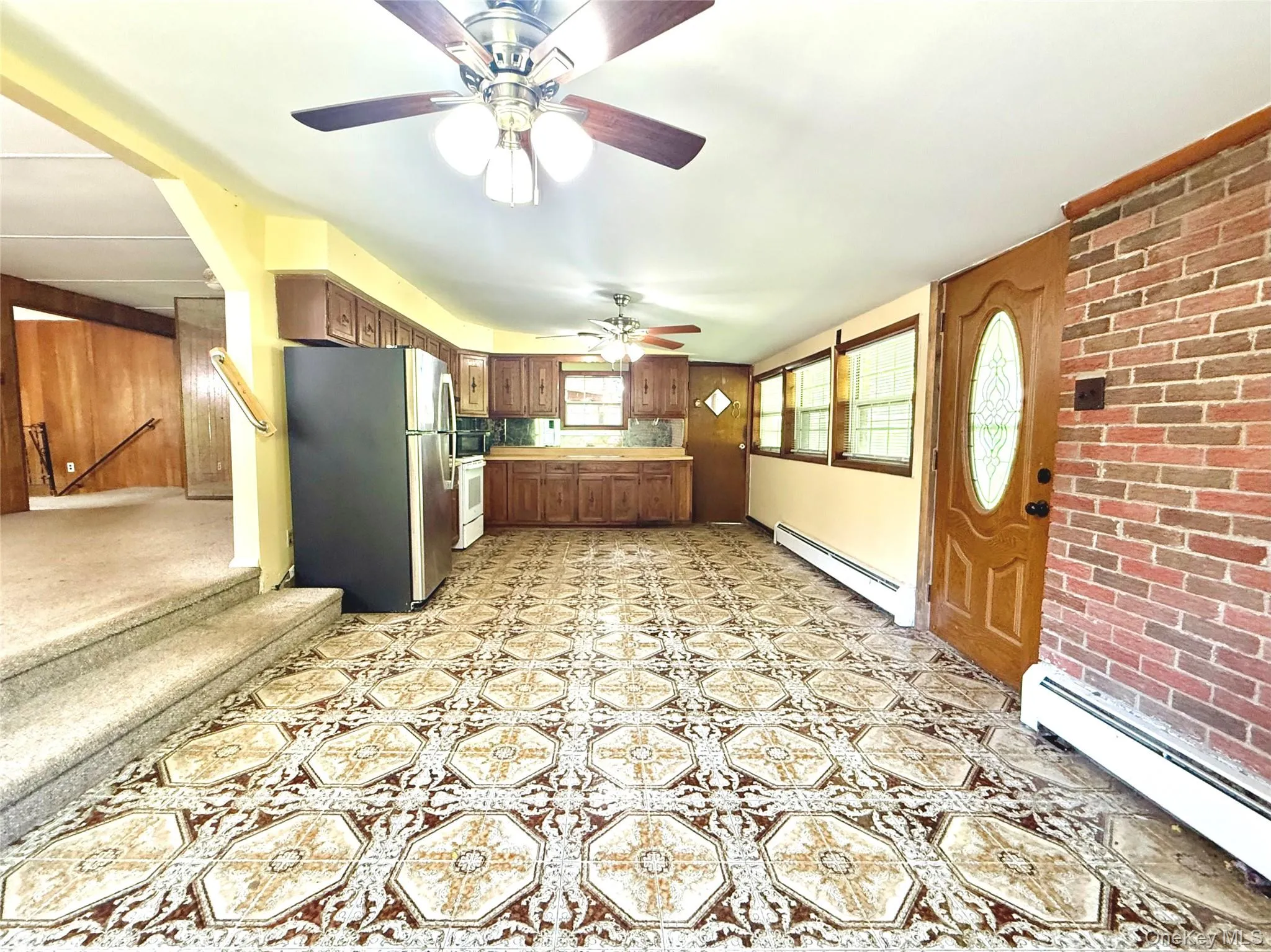 Kitchen with freestanding refrigerator, a baseboard radiator, a ceiling fan, light countertops, and brick wall Kitchen with freestanding refrigerator, a baseboard radiator, a ceiling fan, light countertops, and brick wall