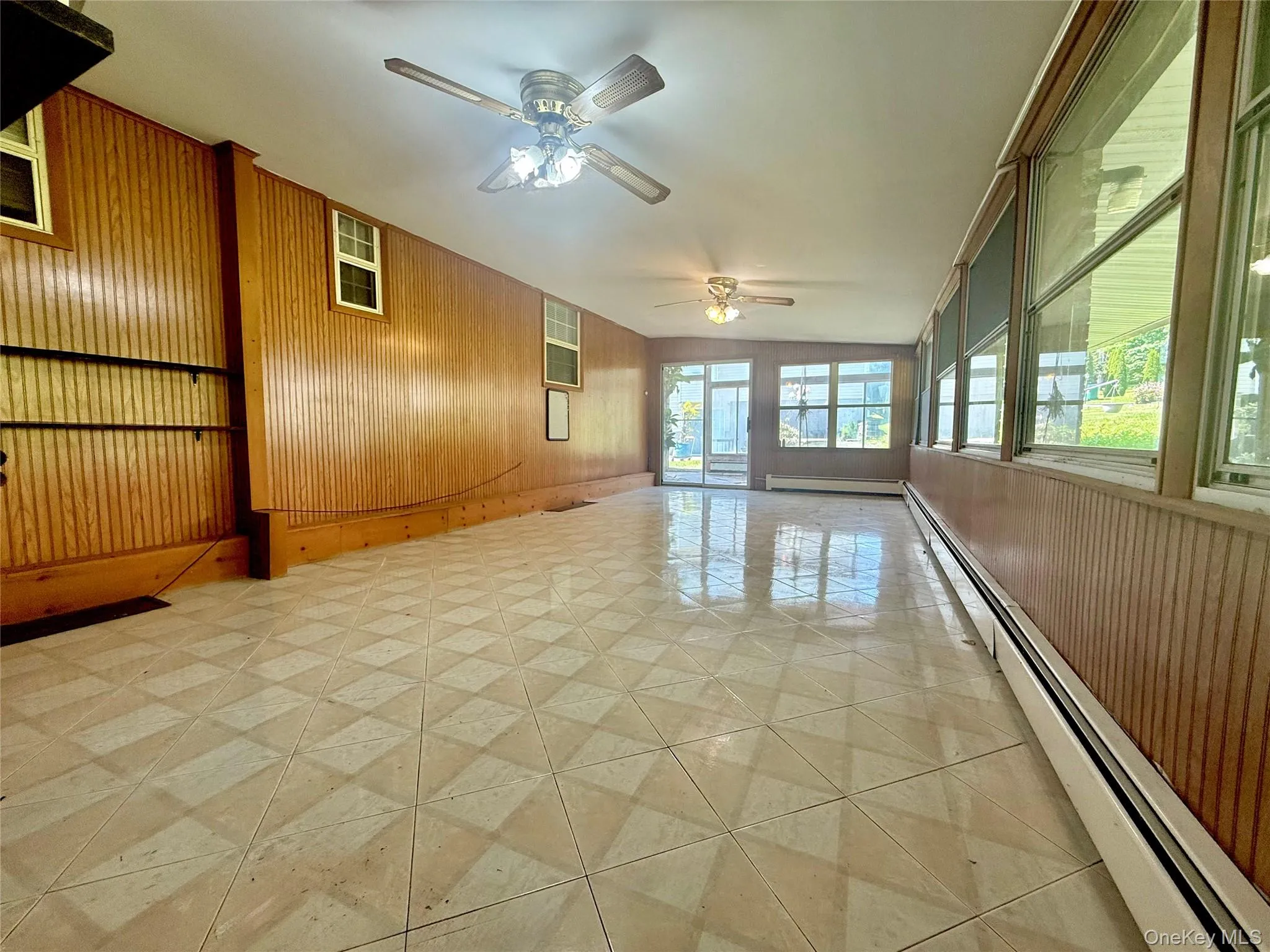 Spare room with a baseboard radiator, wood walls, and ceiling fan Spare room with a baseboard radiator, wood walls, and ceiling fan