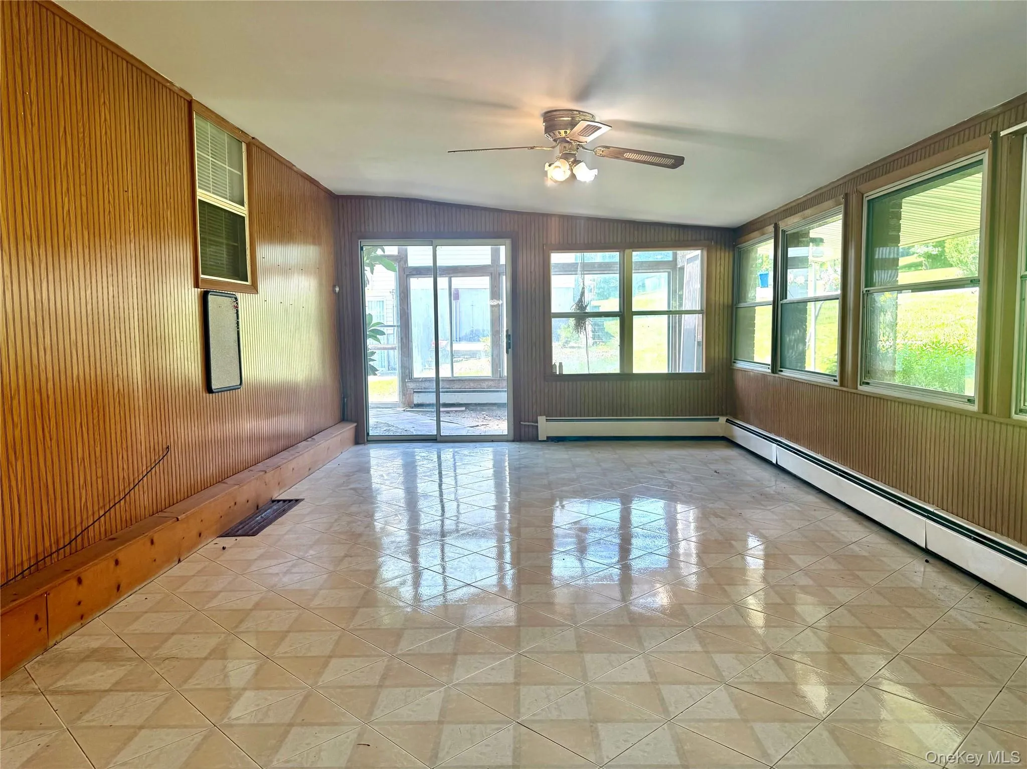 Unfurnished room with ceiling fan, wooden walls, and a baseboard heating unit Unfurnished room with ceiling fan, wooden walls, and a baseboard heating unit