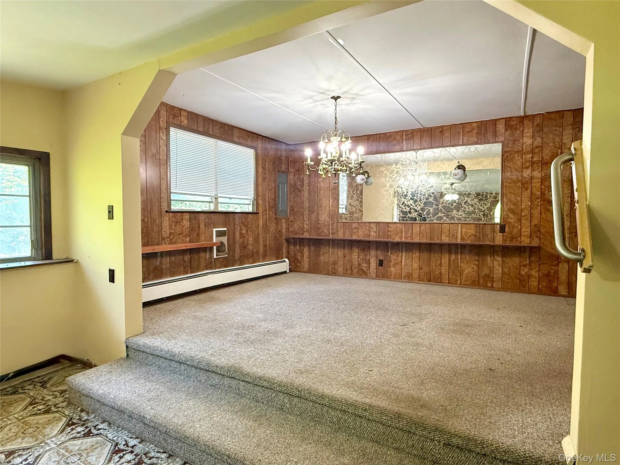 Unfurnished dining area with a baseboard radiator, wood walls, carpet flooring, and a chandelier Unfurnished dining area with a baseboard radiator, wood walls, carpet flooring, and a chandelier