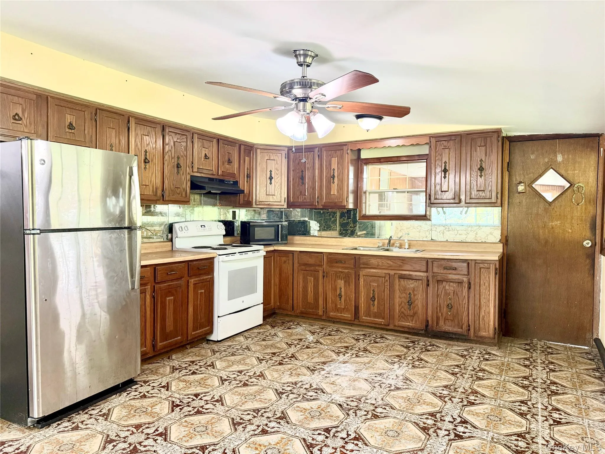 Kitchen featuring appliances with stainless steel finishes, under cabinet range hood, a sink, light countertops, and tasteful backsplash Kitchen featuring appliances with stainless steel finishes, under cabinet range hood, a sink, light countertops, and tasteful backsplash