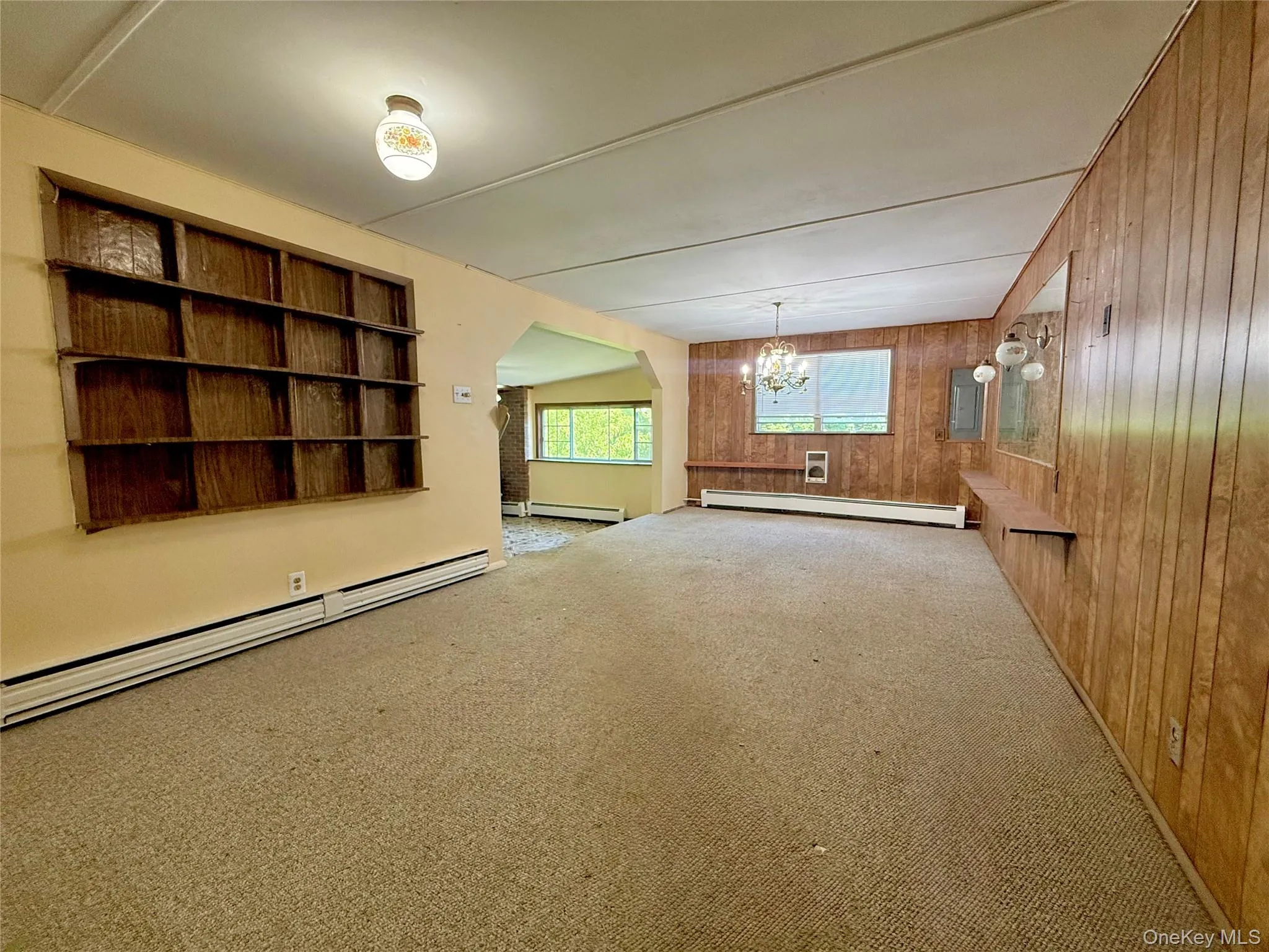 Unfurnished room with a baseboard radiator, wood walls, a chandelier, a baseboard heating unit, and carpet floors Unfurnished room with a baseboard radiator, wood walls, a chandelier, a baseboard heating unit, and carpet floors