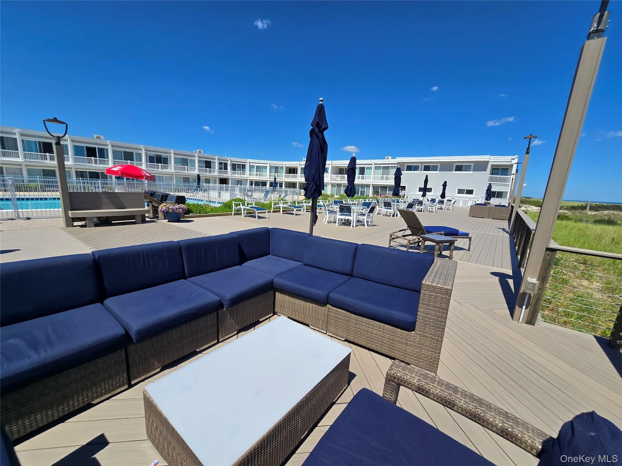 Spacious outdoor deck area featuring a large sectional seating unit, a white rectangular coffee table, and a protective railing Spacious outdoor deck area featuring a large sectional seating unit, a white rectangular coffee table, and a protective railing