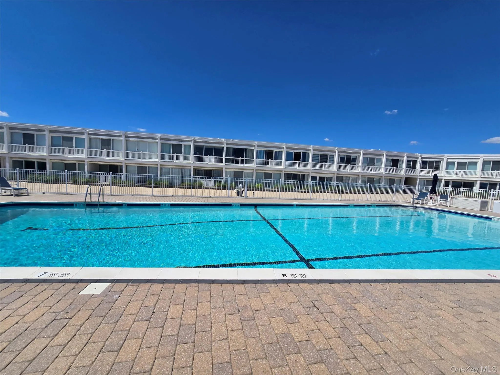 Community swimming pool featuring a perimeter fence and a surrounding paver patio Community swimming pool featuring a perimeter fence and a surrounding paver patio