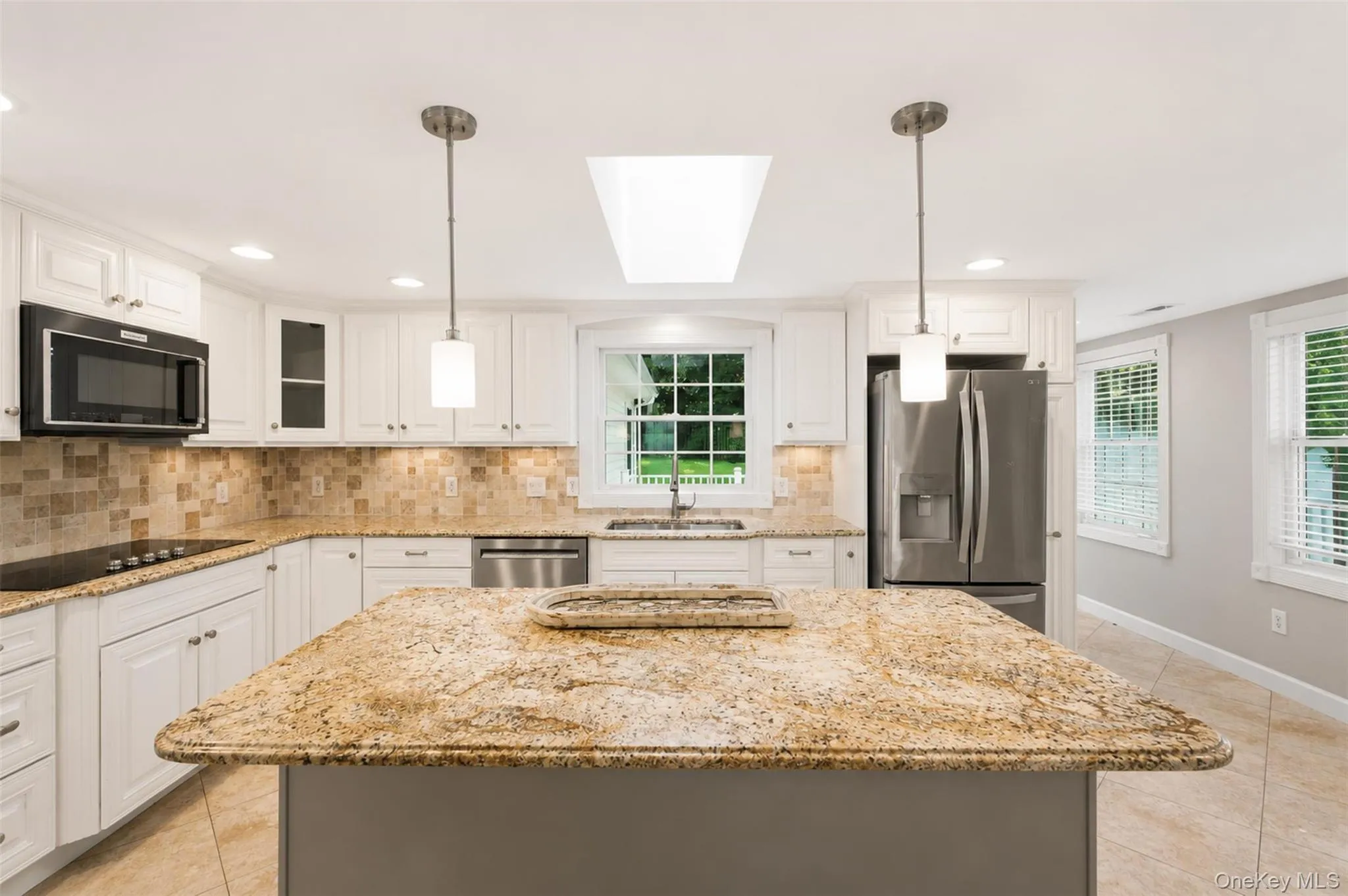 Kitchen featuring a central island with a stone countertop, white cabinetry, integrated stainless steel appliances, a tile backsplash, and recessed lighting Kitchen featuring a central island with a stone countertop, white cabinetry, integrated stainless steel appliances, a tile backsplash, and recessed lighting